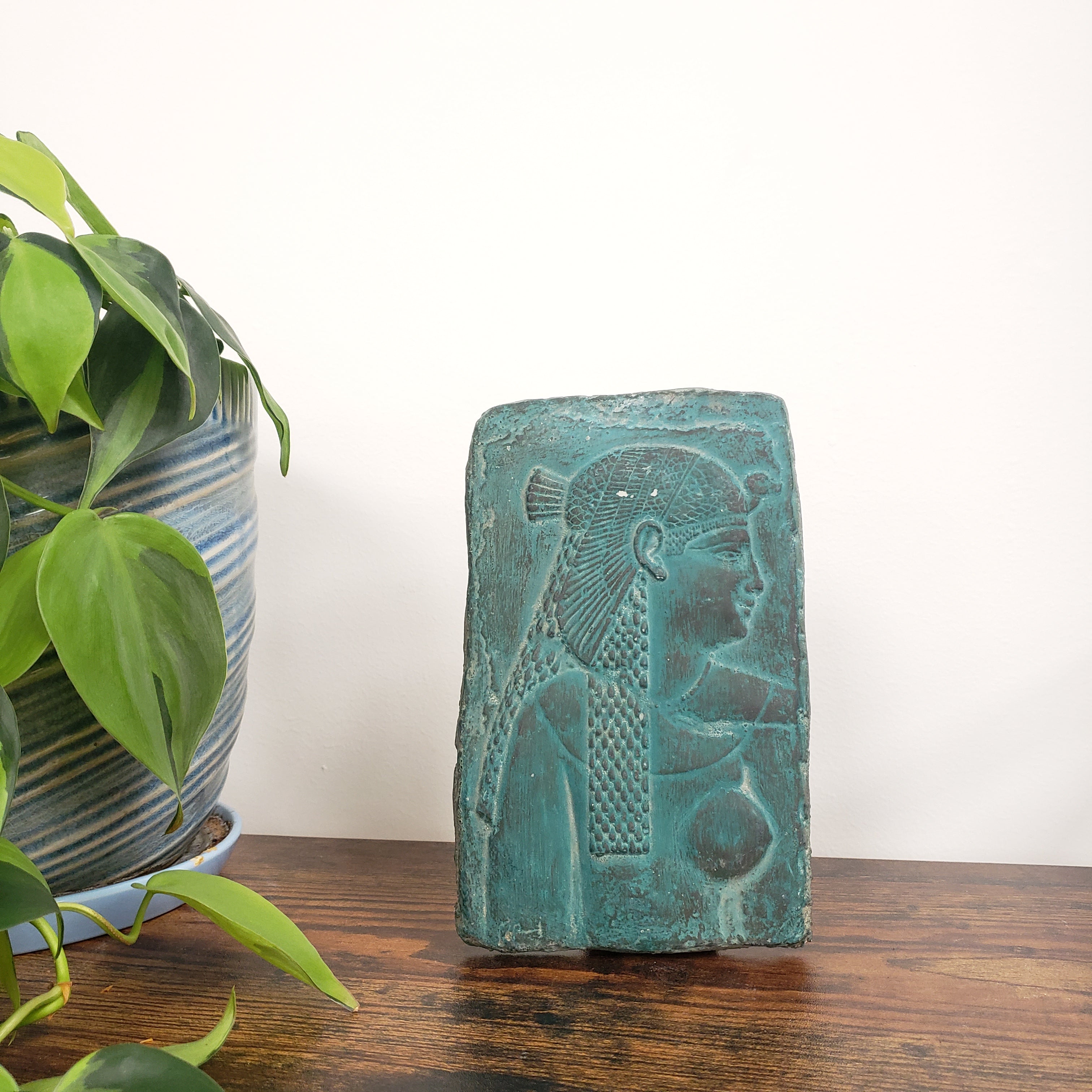 Decorative Cleopatra wall hanging on a white wall with plants in the foreground