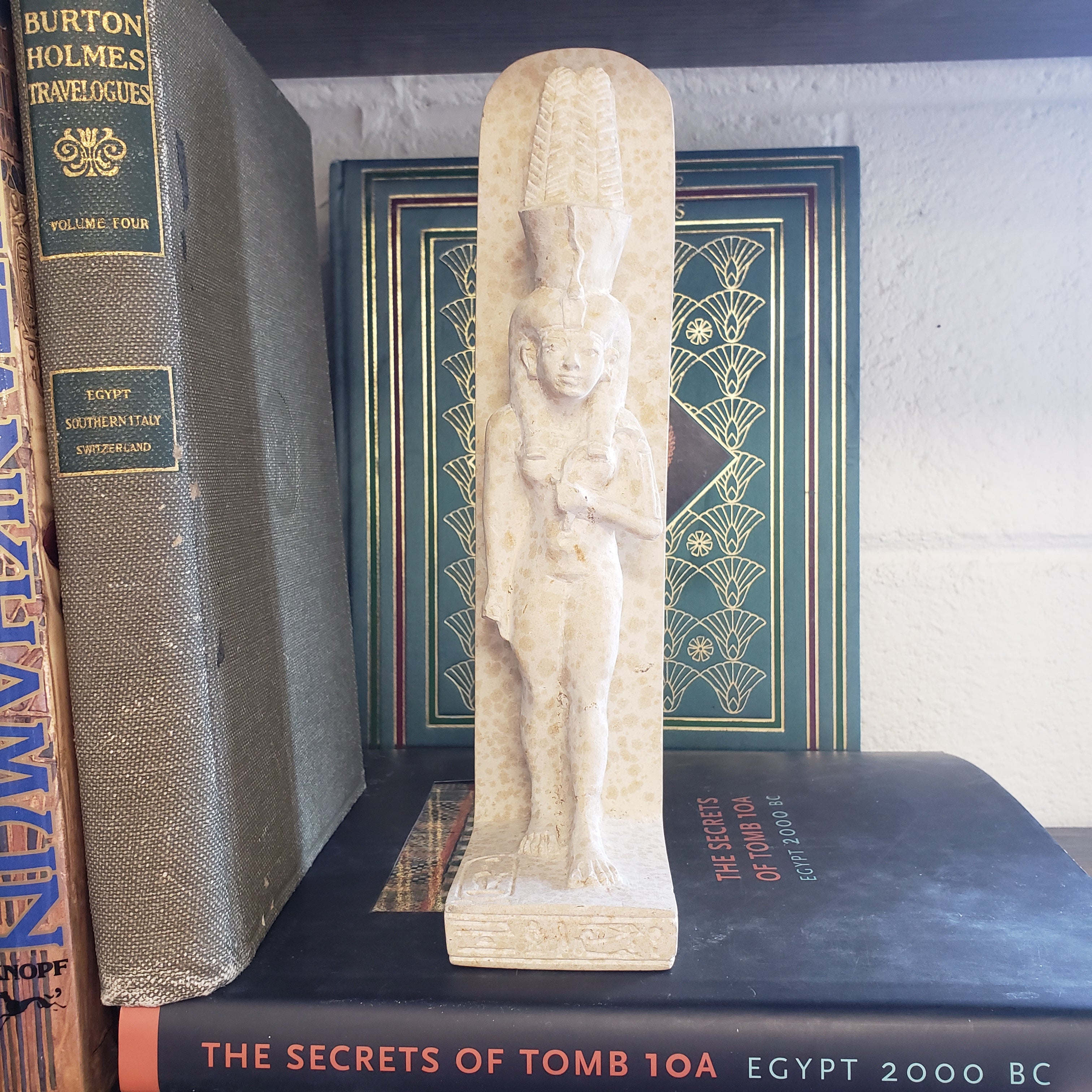 Decorative statue of Tiye on top of books with visible titles.