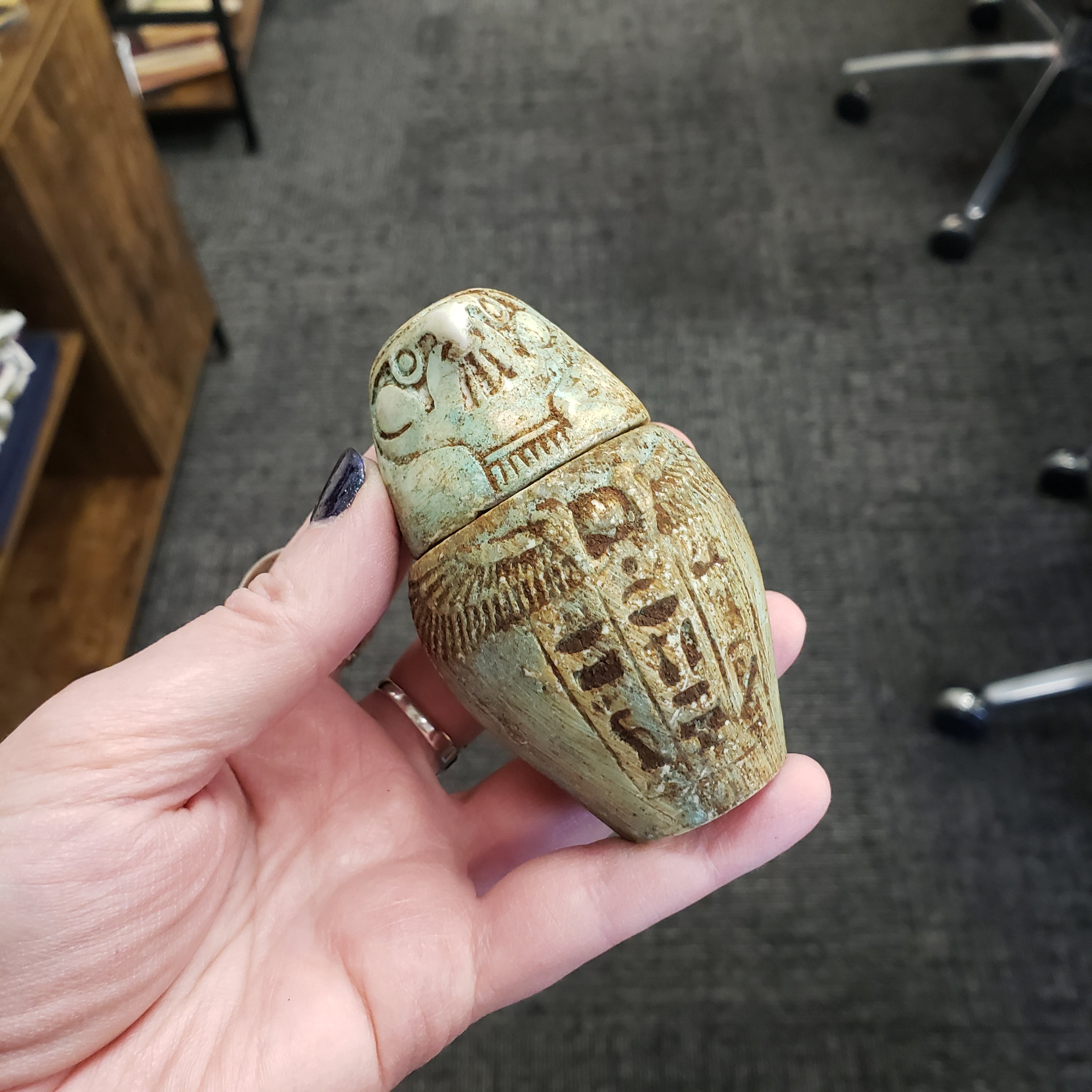 Hand holding a decorative stone object with intricate carvings against an indoor background
