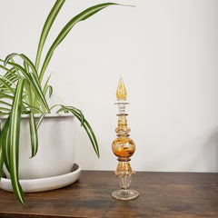Decorative glass perfume bottle with a plant and white container on a wooden surface.