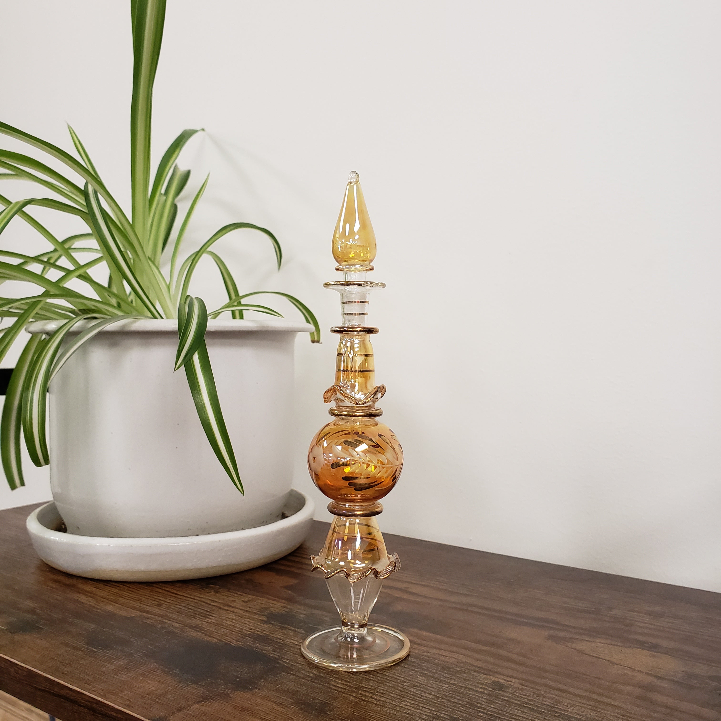 Decorative glass perfume bottle on a wooden surface with a plant in the foreground