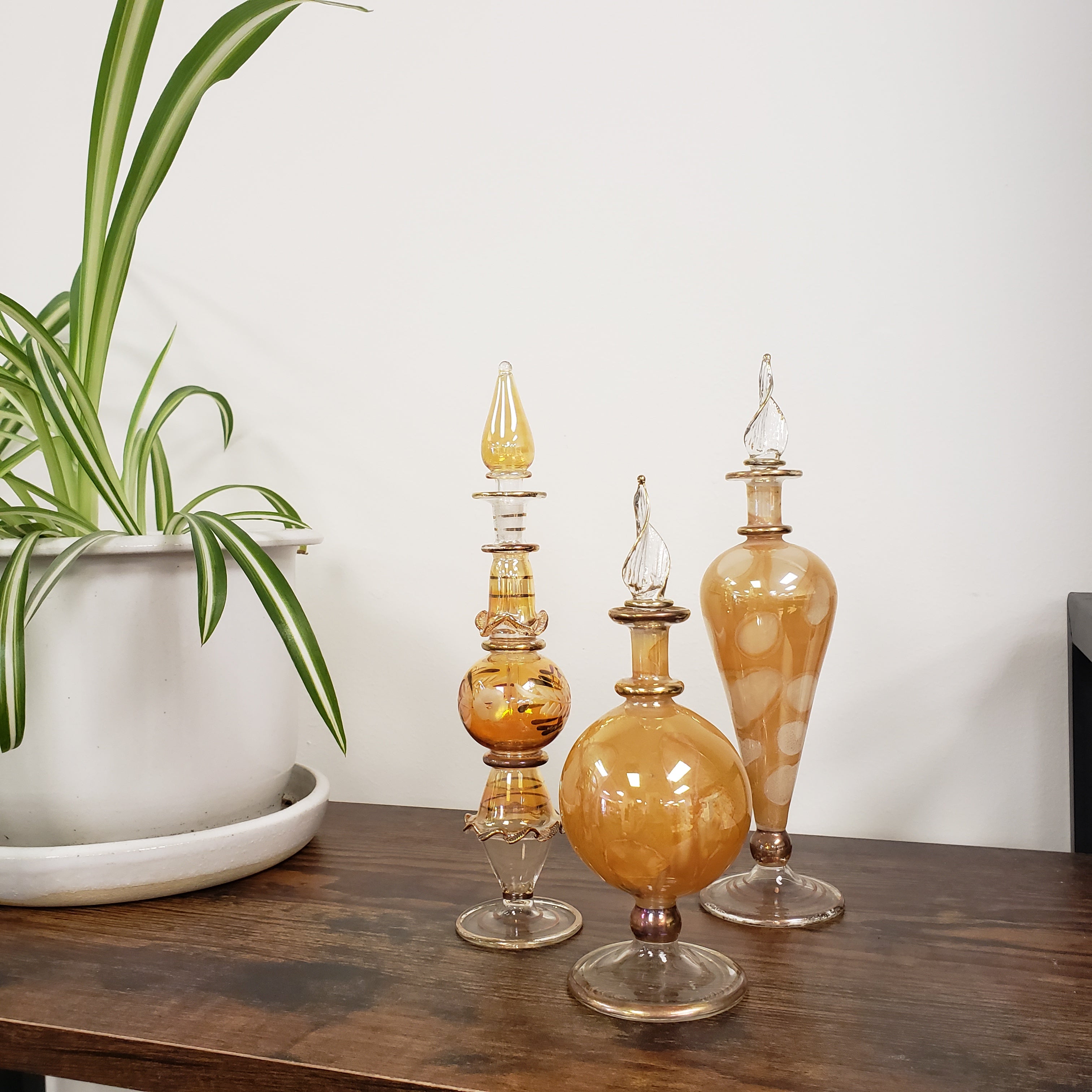 Set of three amber-colored glass lamps on a wooden surface with a plant in the foreground.