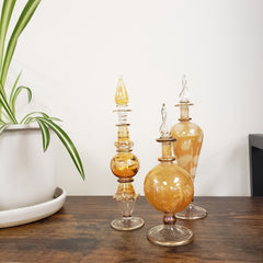 Set of amber glass bottles on a wooden surface with a white wall and plant in the background