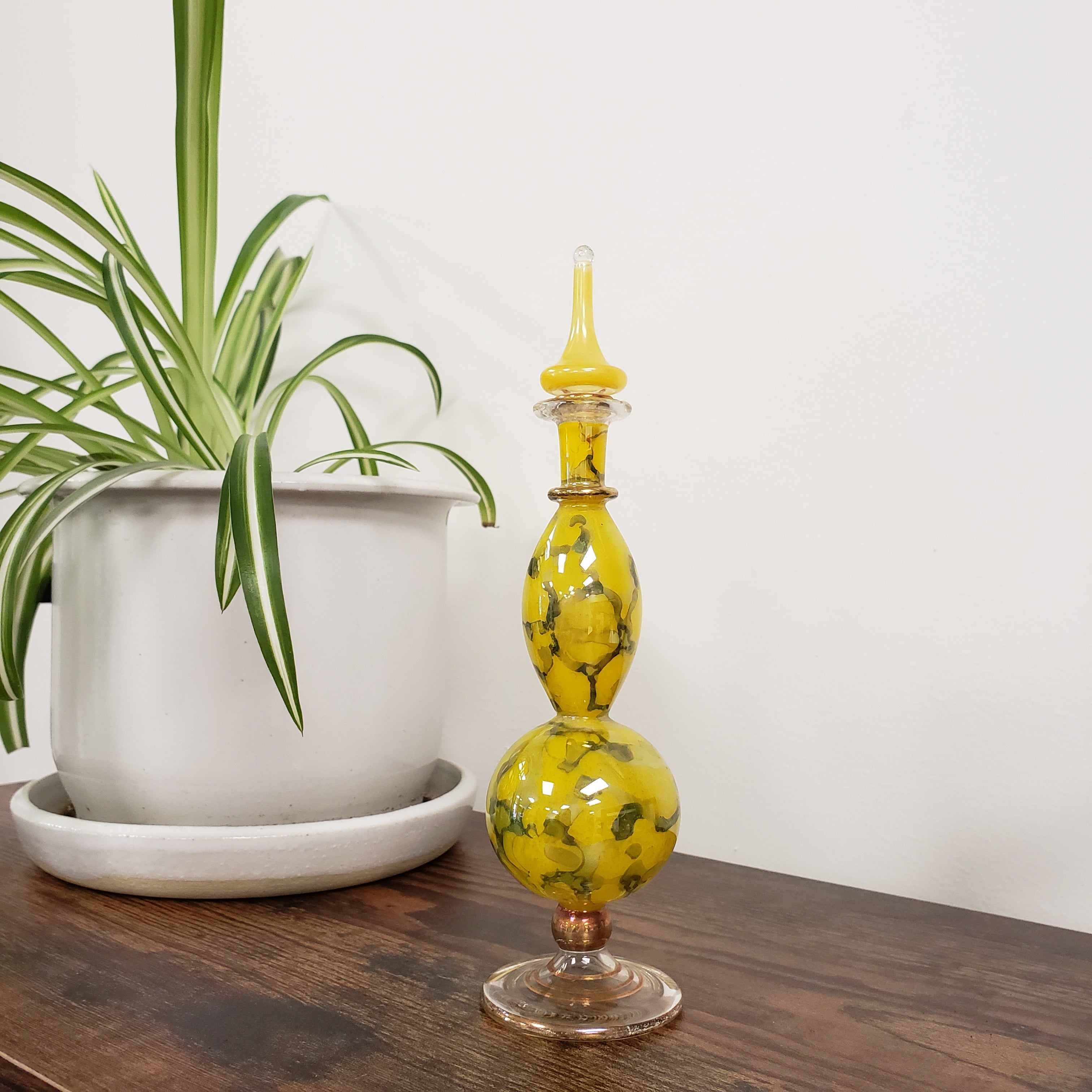 Decorative yellow glass perfume bottle on a wooden surface with a plant in the foreground.