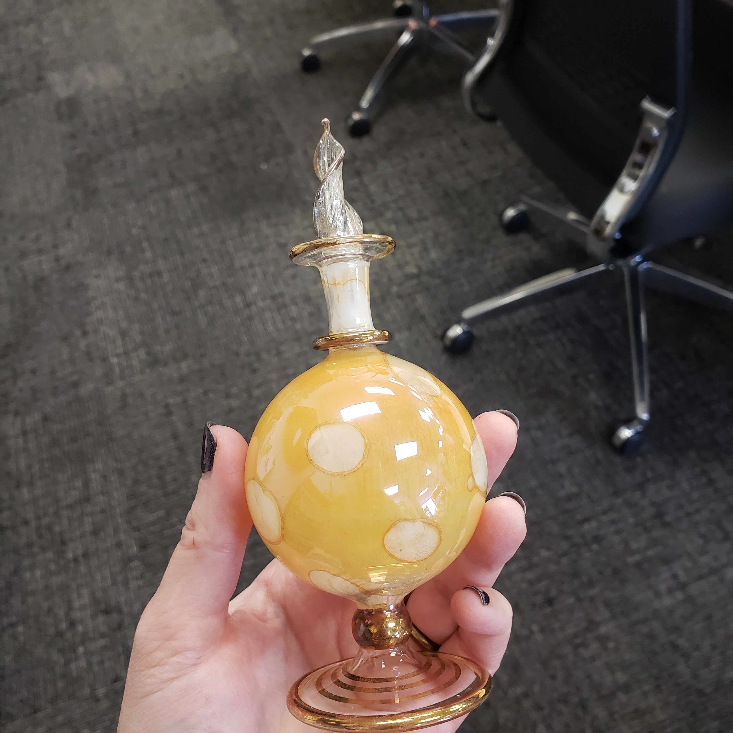 Hand holding a decorative glass object with a yellow sphere and gold accents on a carpeted floor.