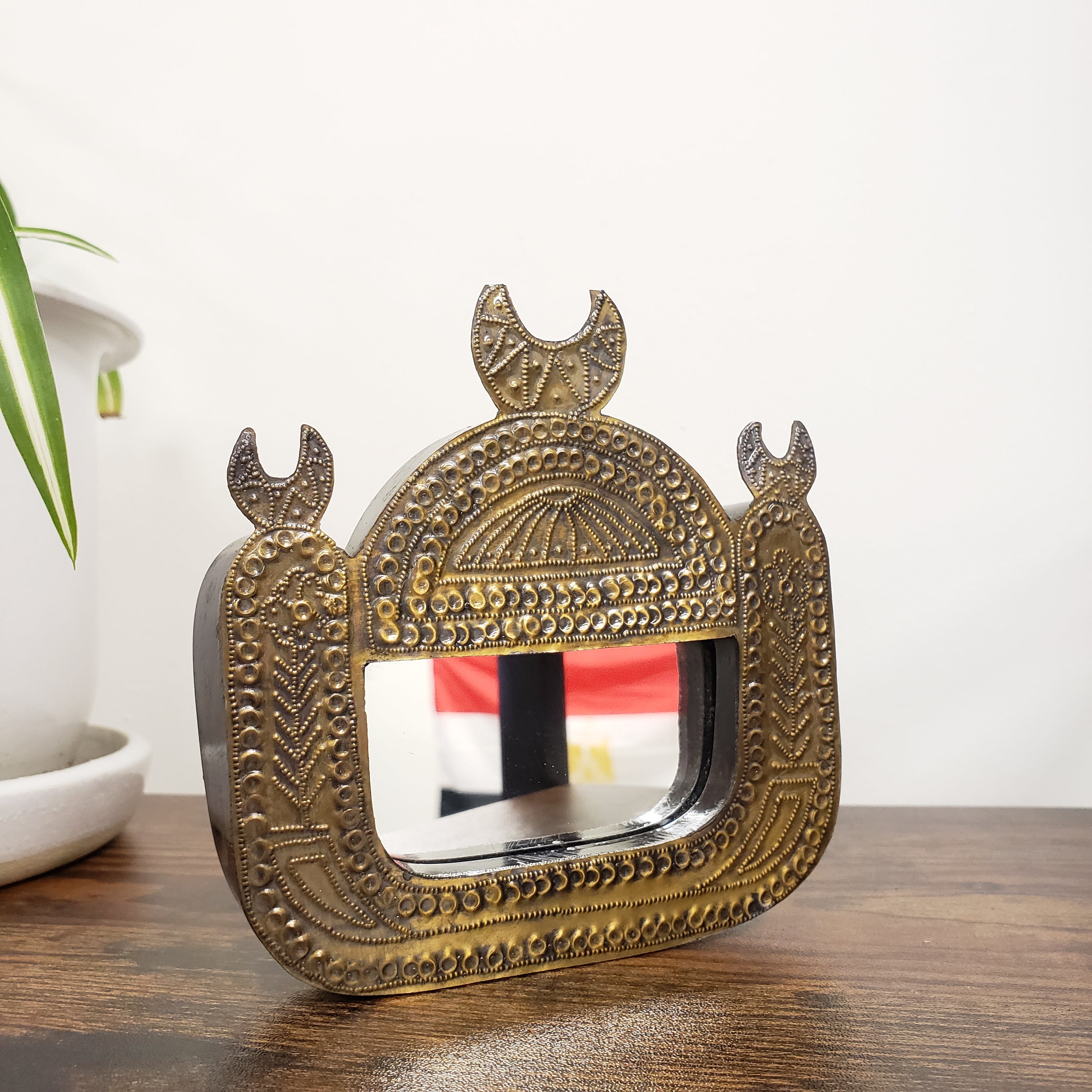 Decorative wall mirror with intricate gold frame on a white wall.