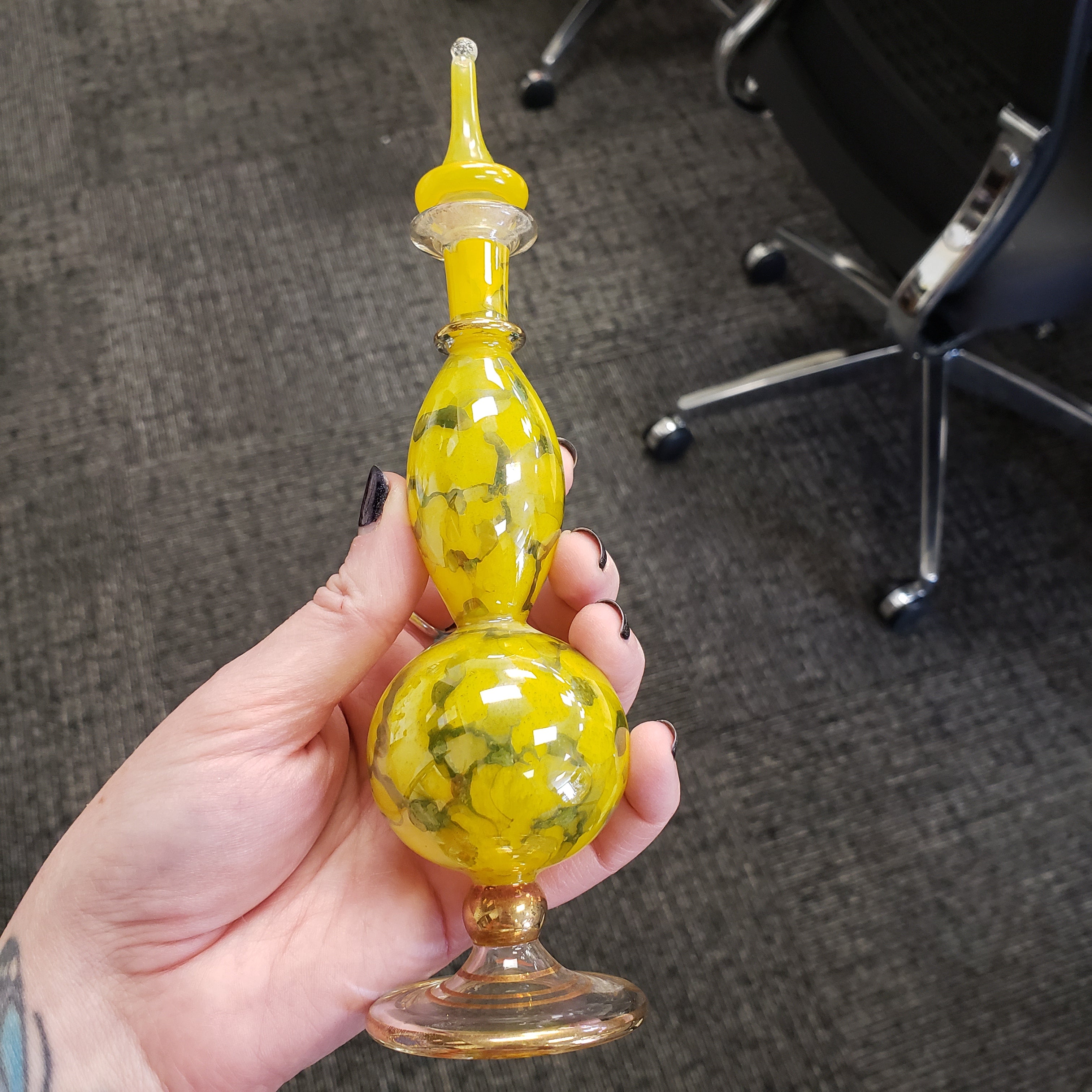 Hand holding a yellow glass perfume bottle with intricate design on a textured surface.