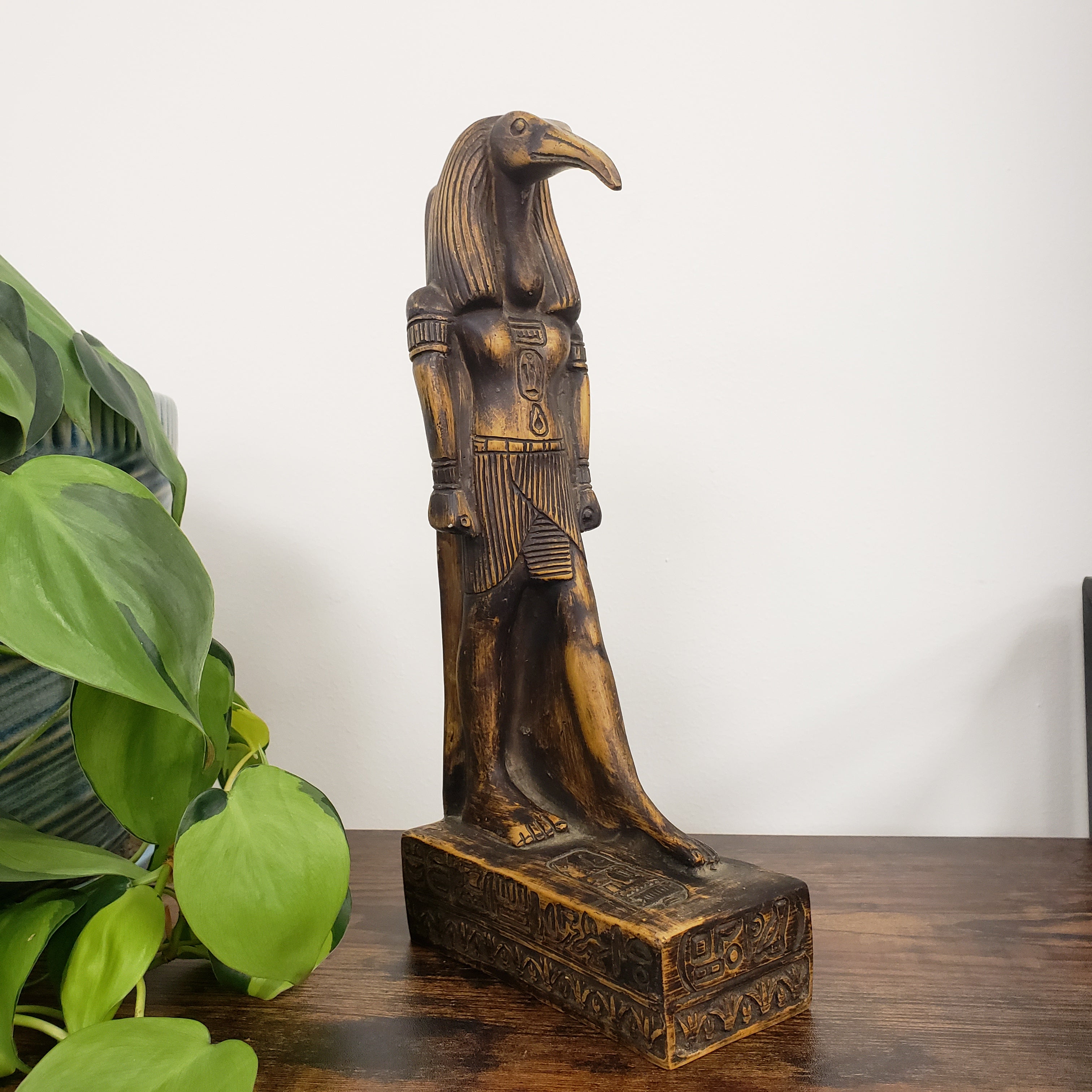 Decorative Egyptian god Thoth sculpture on a wooden block with a plant in the foreground