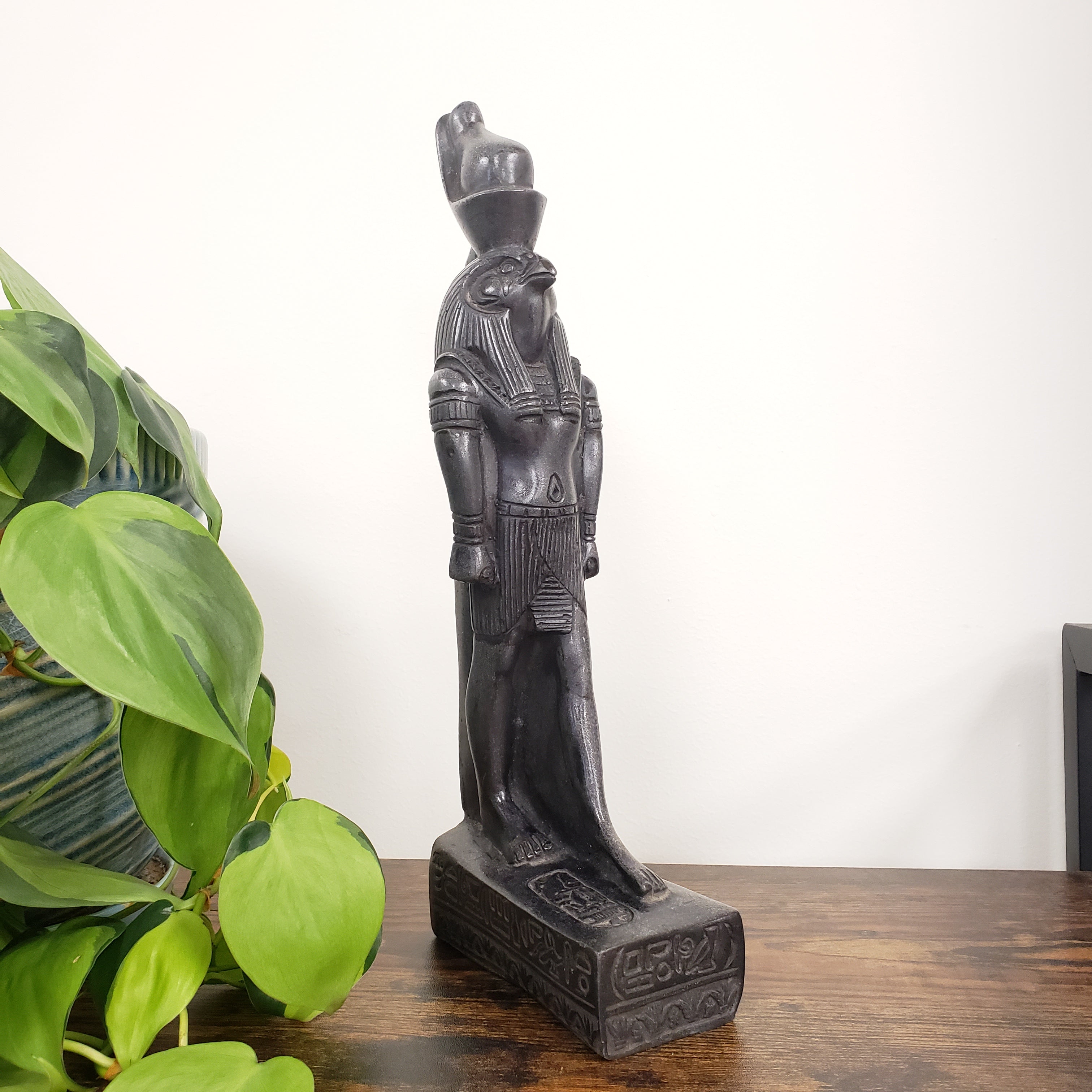 Decorative Egyptian god Ra statue on a wooden surface with a plant in the foreground