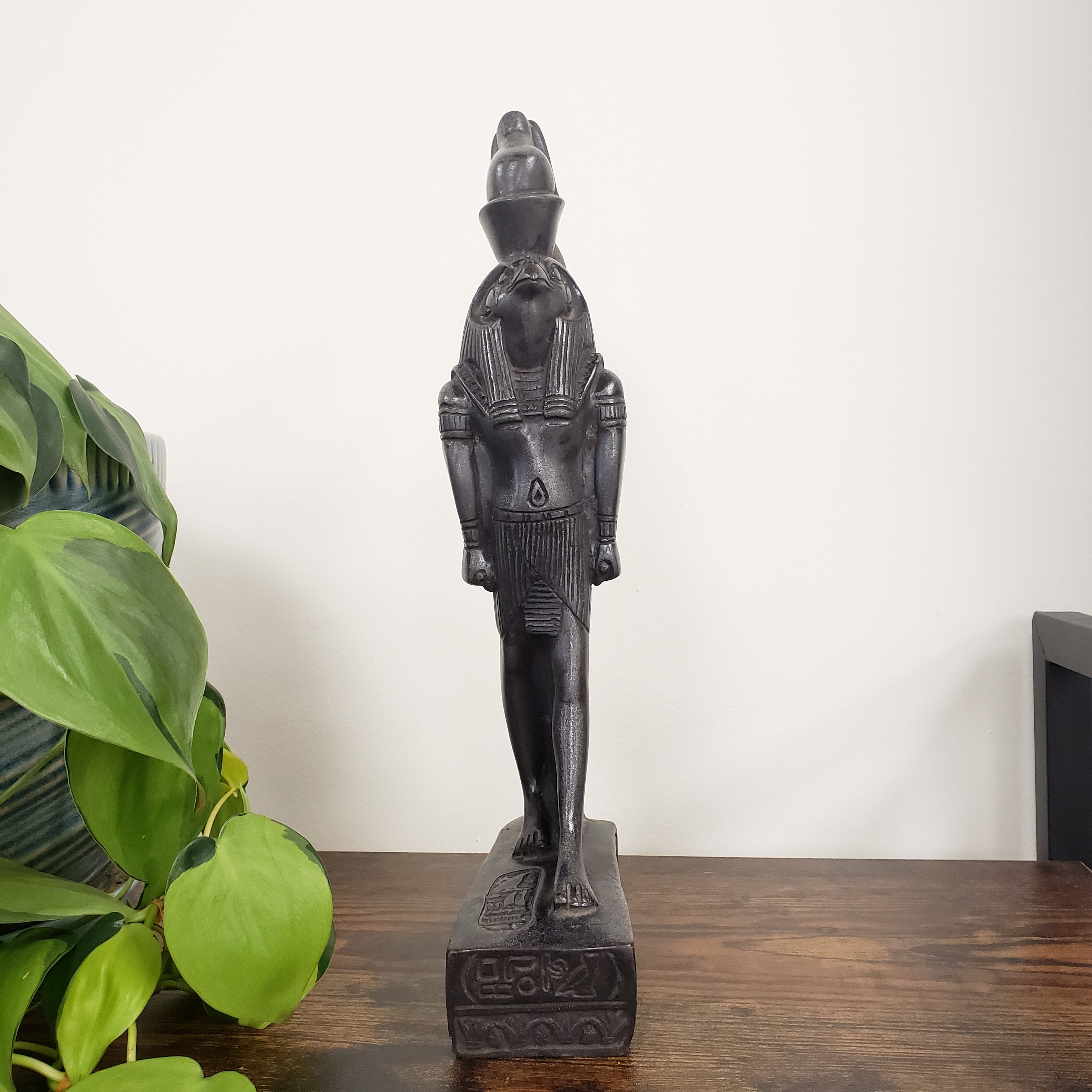 Decorative black statue on a wooden shelf with green leaves in the foreground
