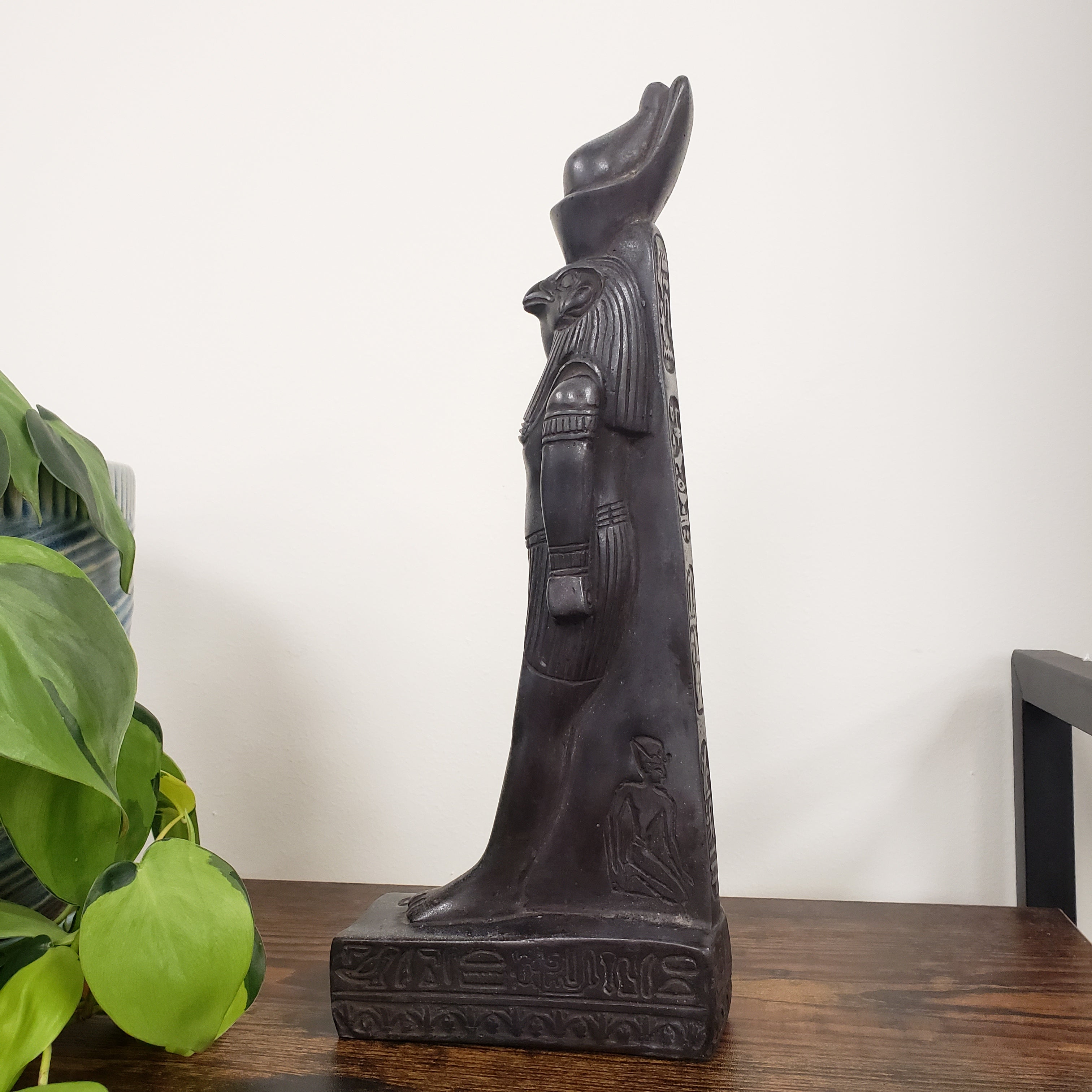 Decorative Egyptian god Ra statue  on a wooden surface with a plant in the foreground.