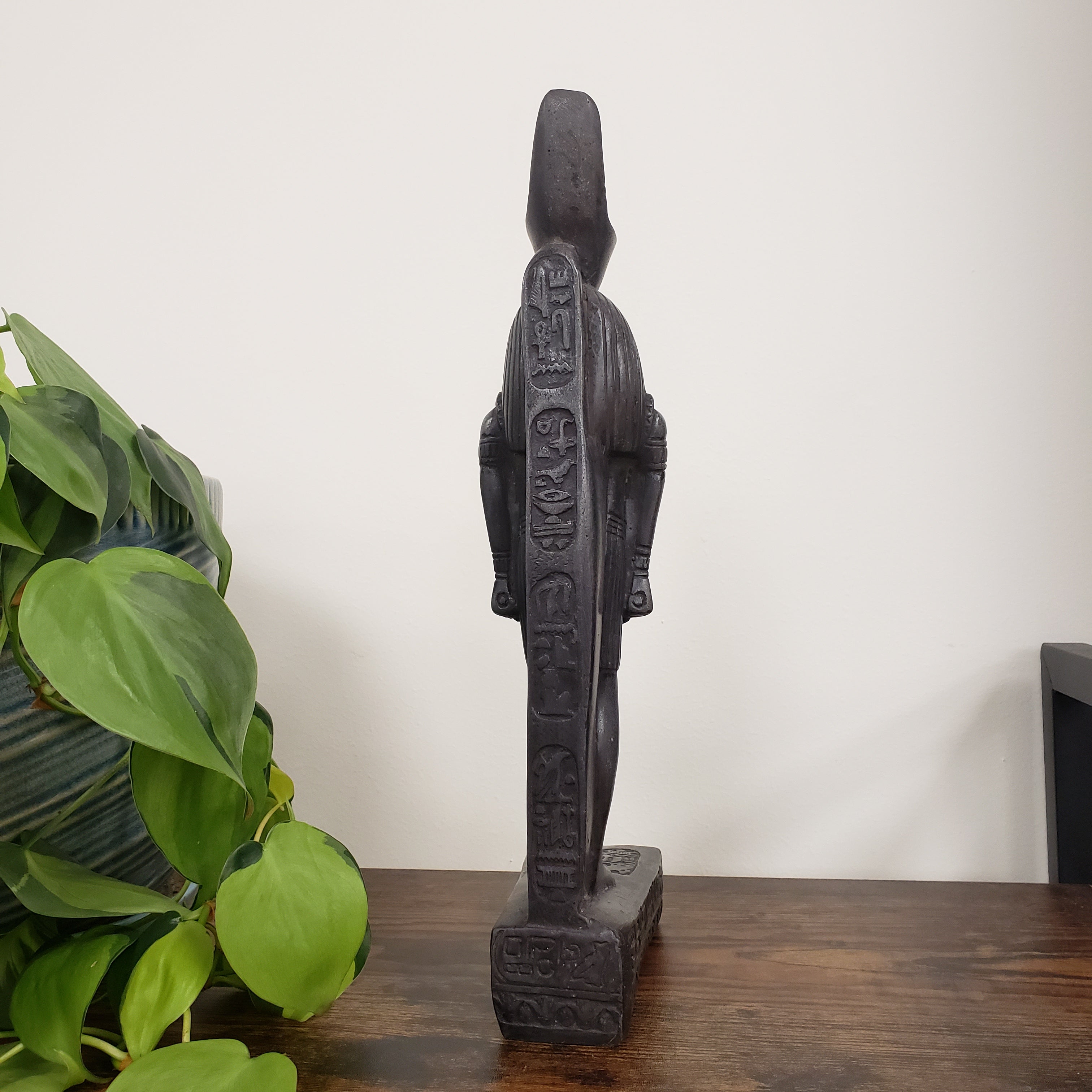 Decorative Egyptian god Ra statue on a white wall with a plant in the foreground