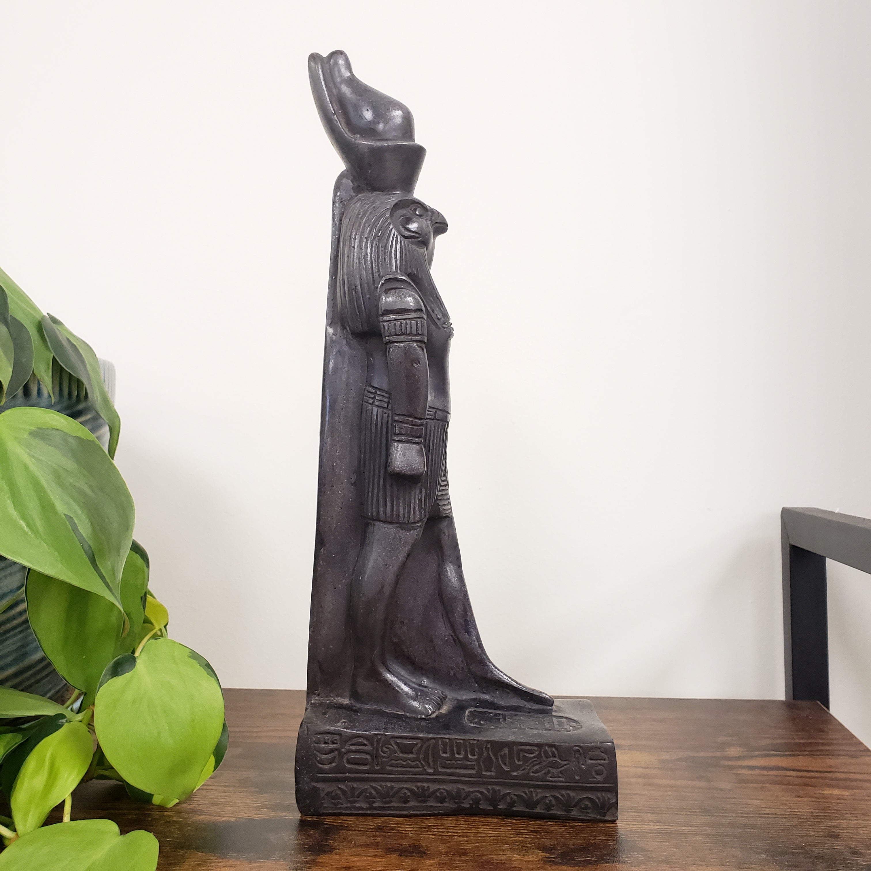 Decorative Egyptian god Ra statue  with intricate designs on a wooden shelf against a white wall.