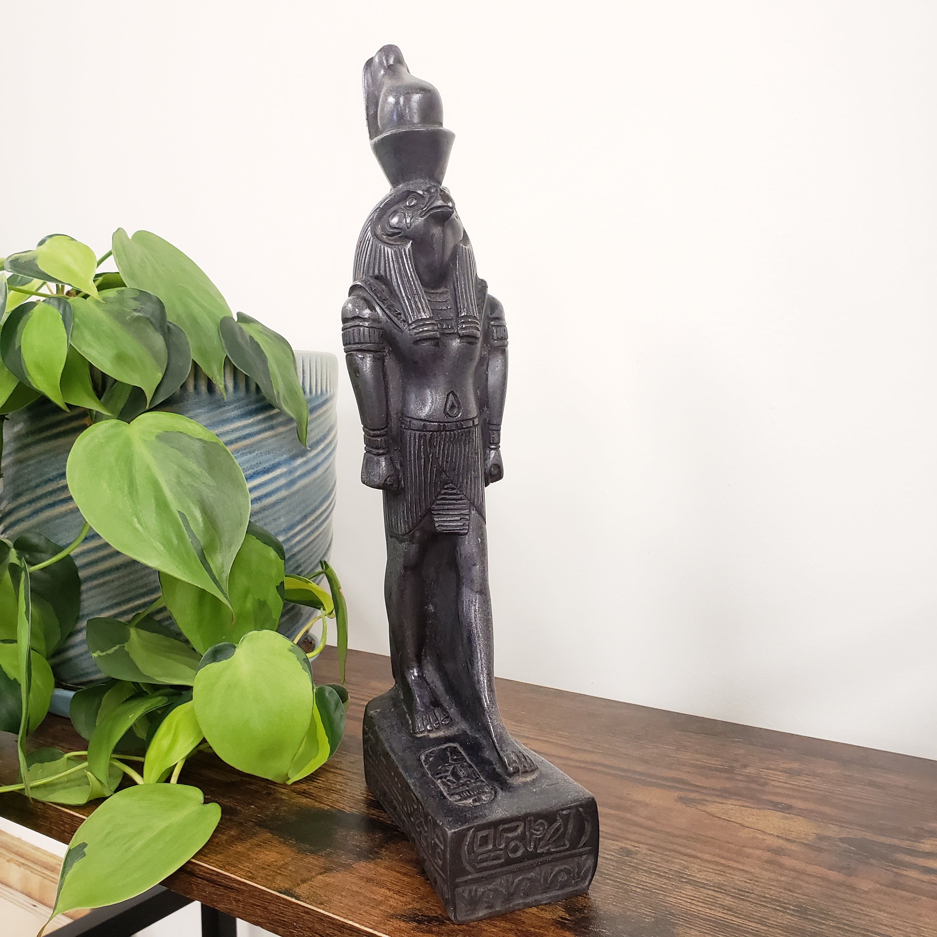 Decorative Egyptian god Ra statue  sculpture on a wooden surface with a plant in the foreground
