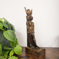 Decorative statue of the Egyptian god Babi with intricate carvings next to a potted plant on a white background