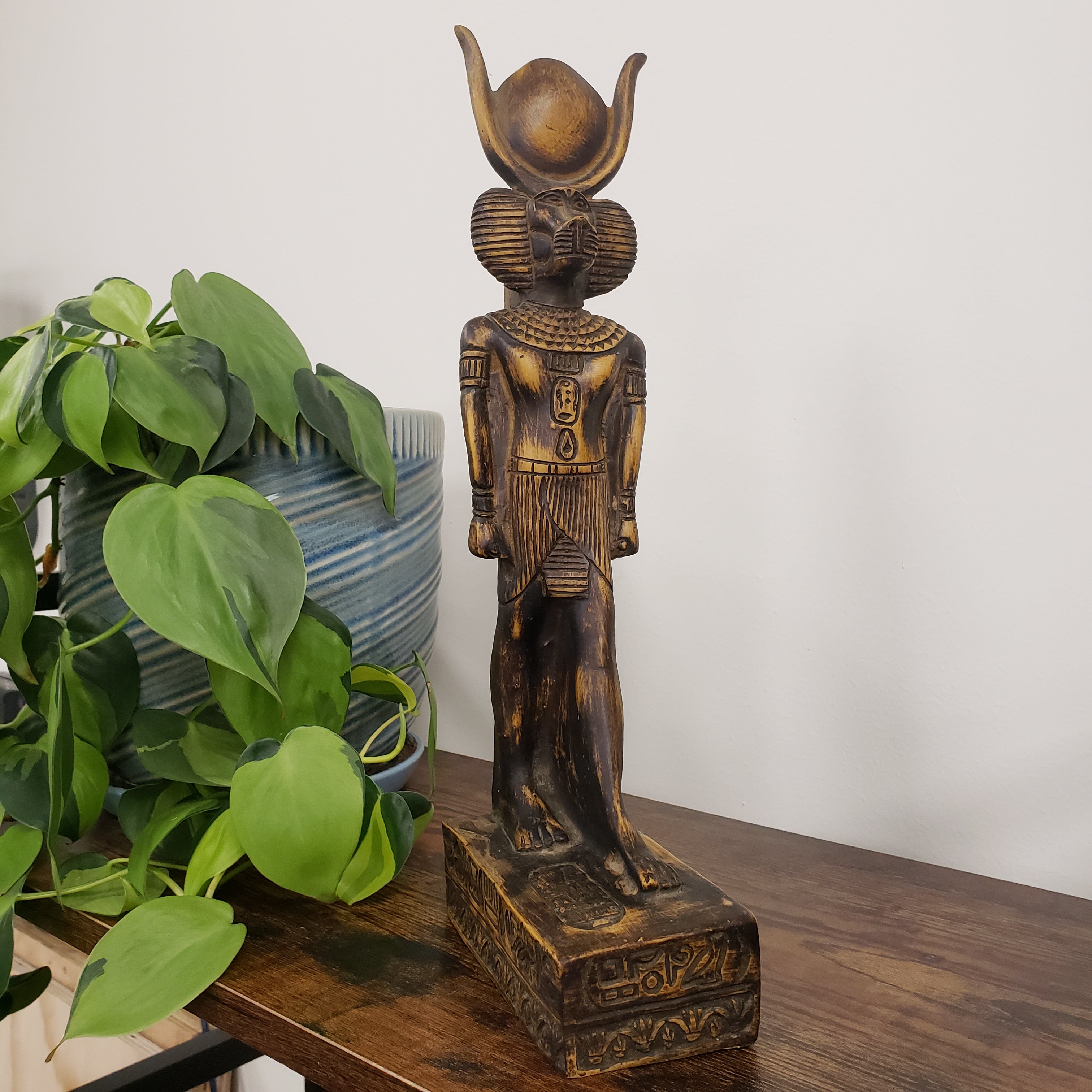 statue of the Egyptian god Babi  on a shelf with plants and a pillow.