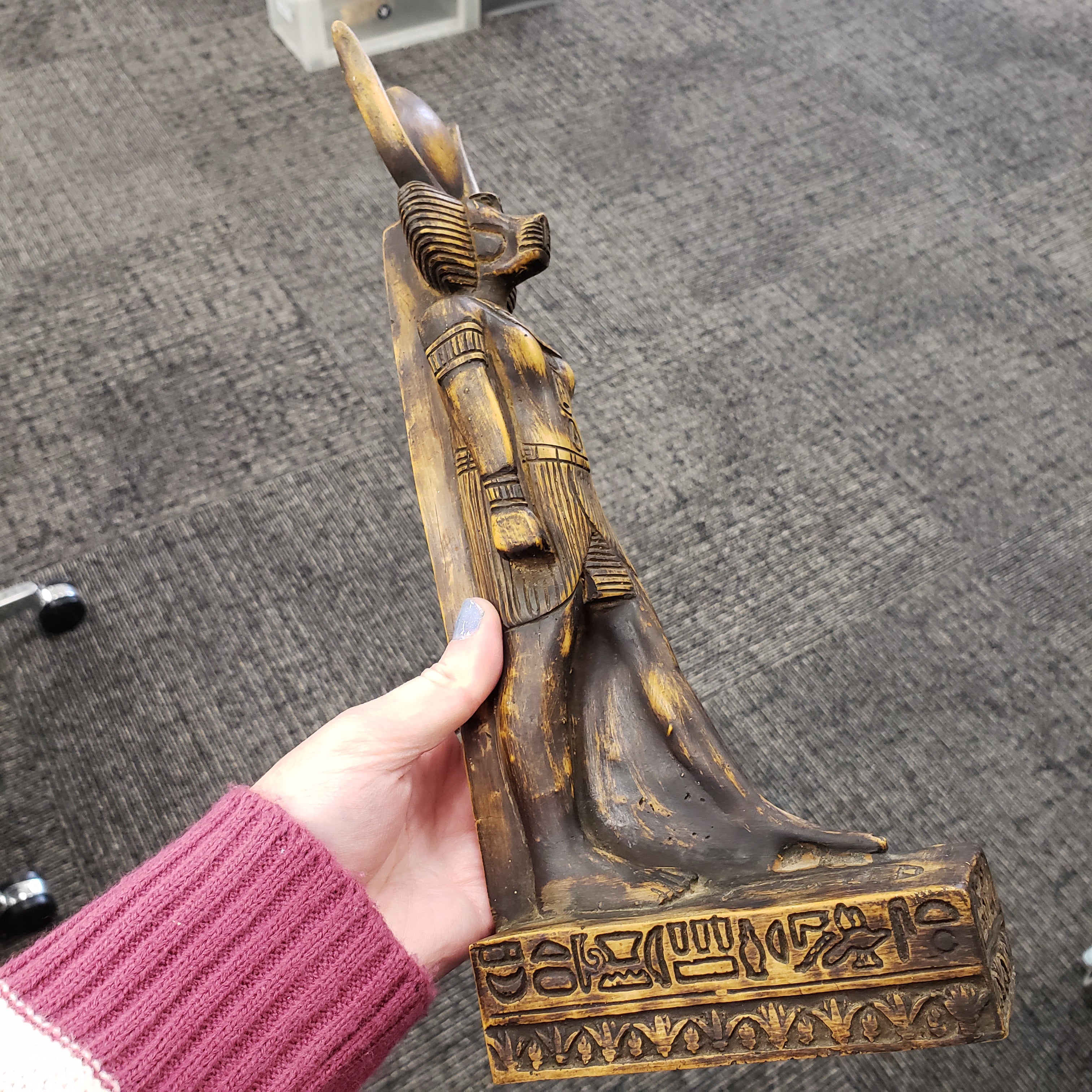 Hand holding a statue of the Egyptian god Babi  with intricate carvings against a gray background
