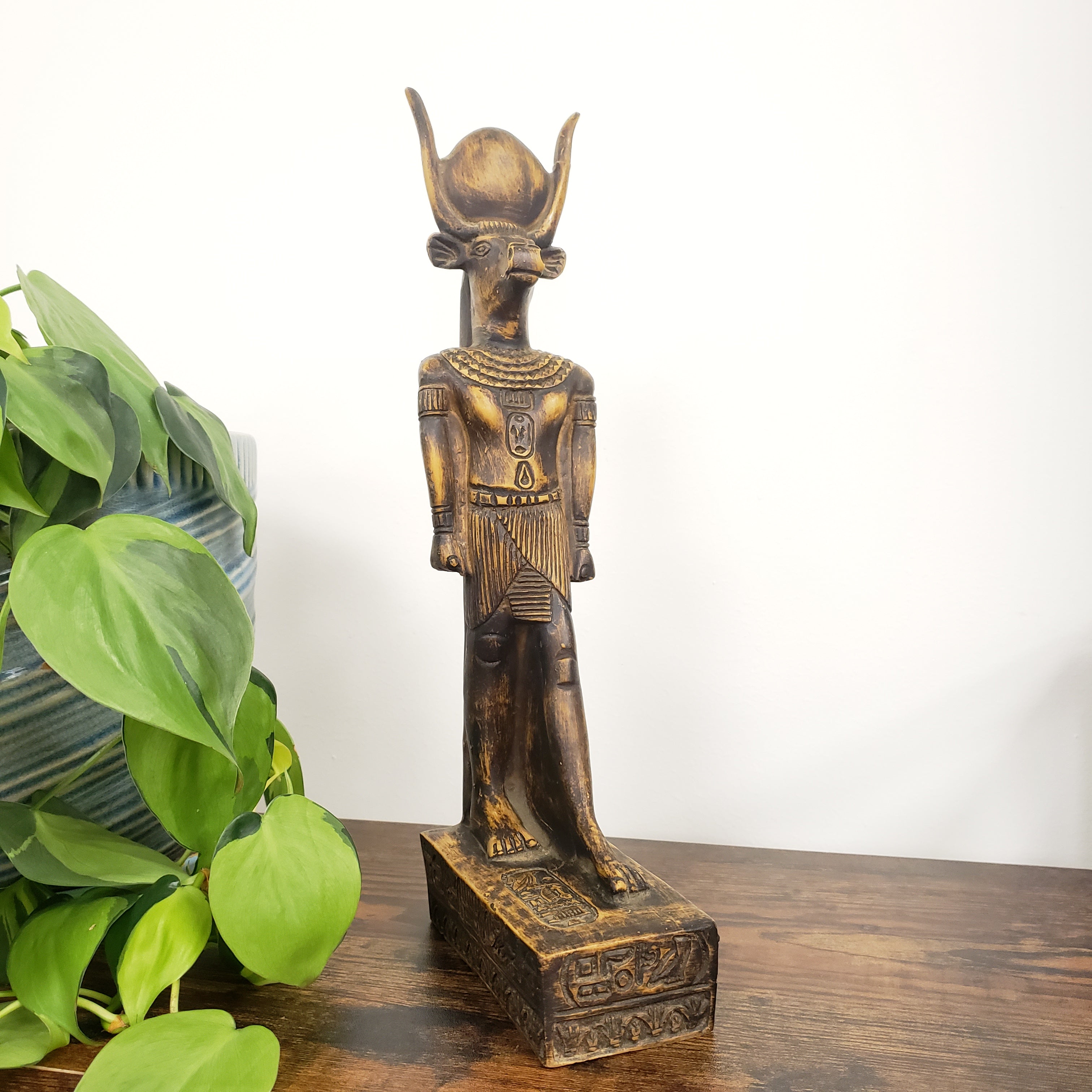 Decorative wooden statue on a white surface with green leaves in the foreground