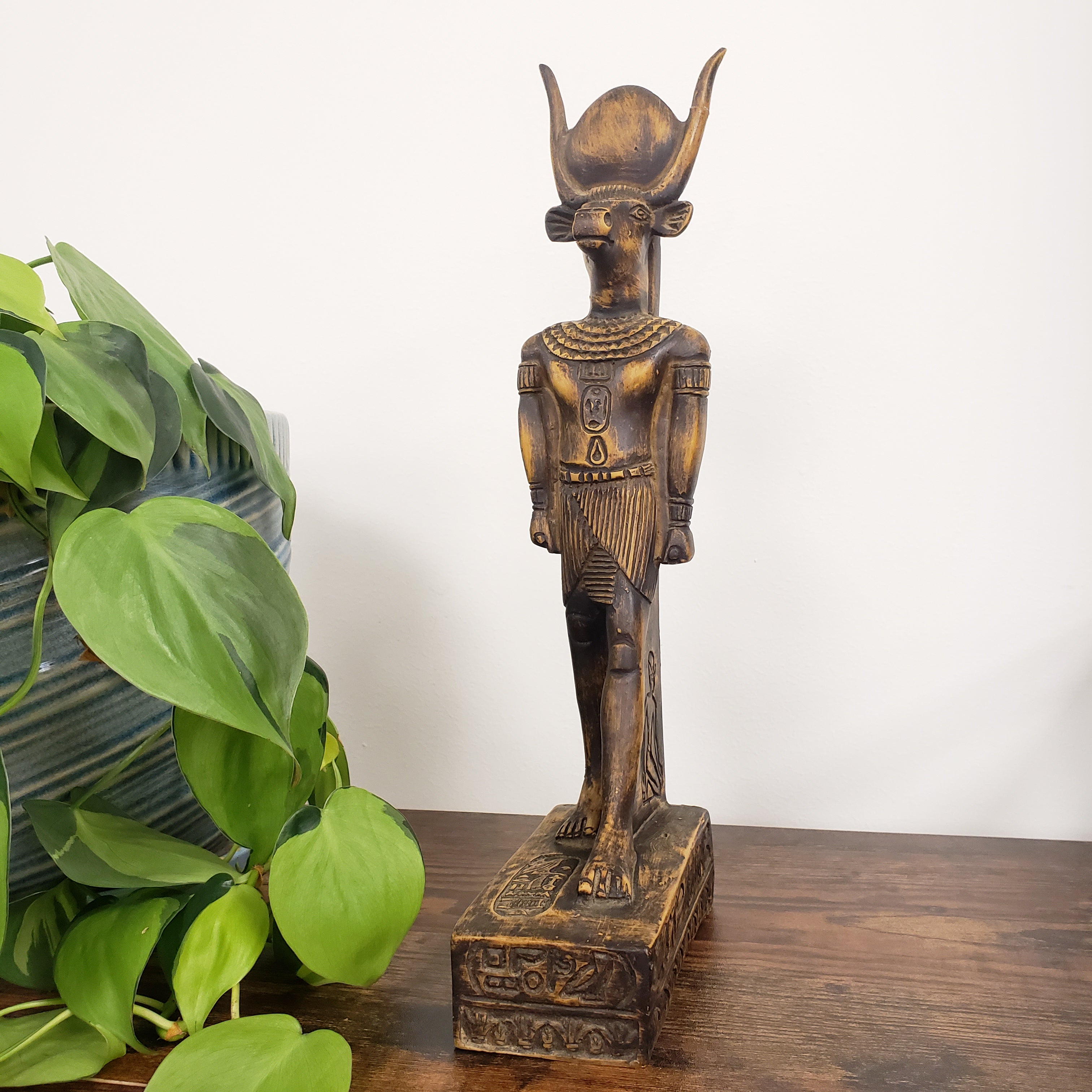 Bronze statue of a deity on a wooden shelf with green plants below