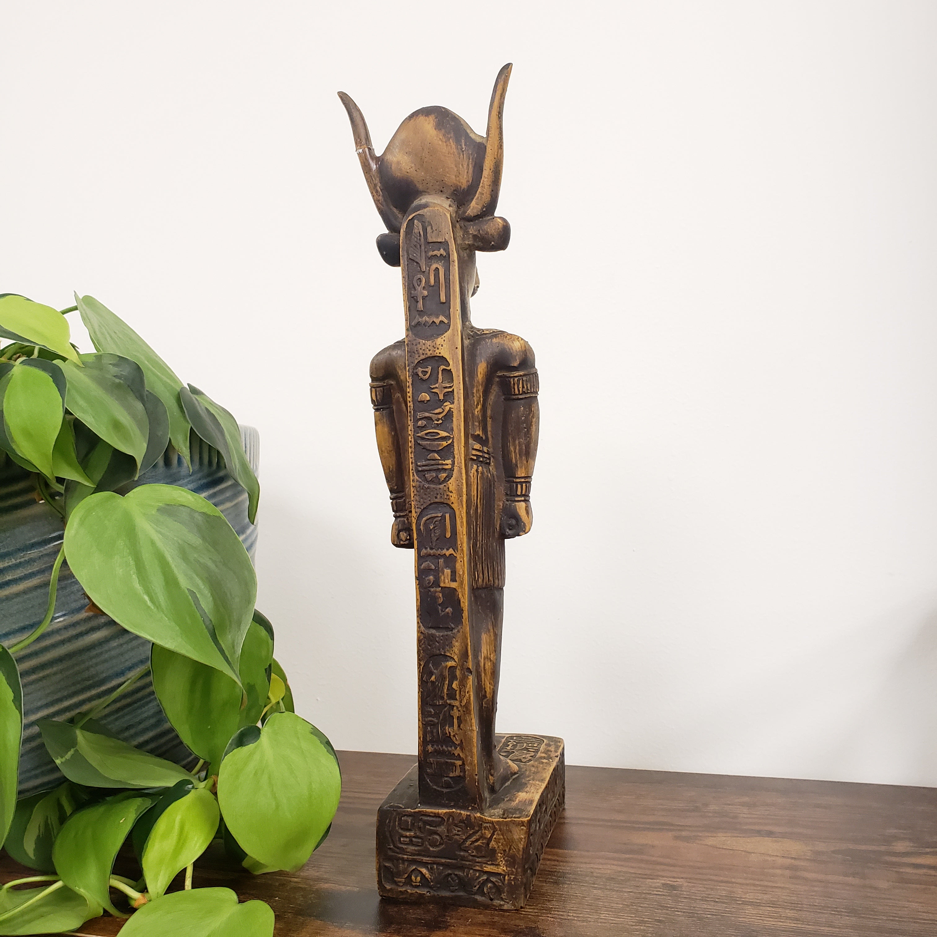 Decorative Egyptian god Montu statue with intricate carvings on a white wall with a plant in the foreground.