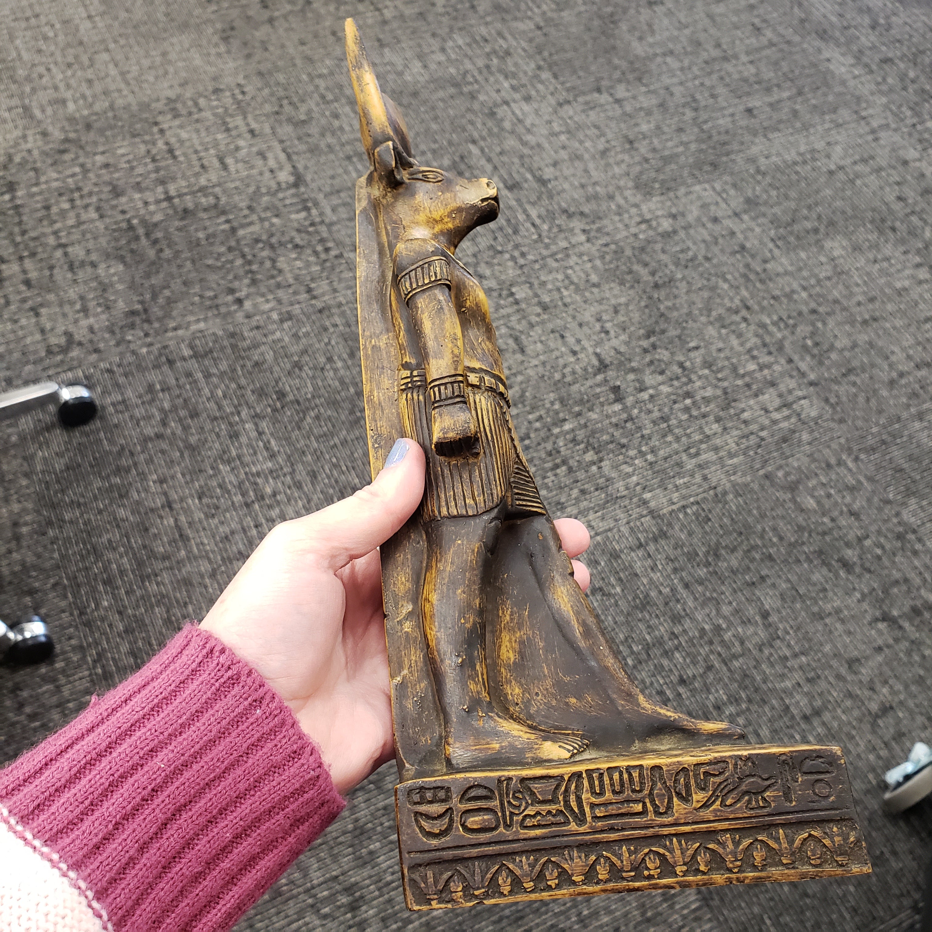 Hand holding a wooden sculpture of Egyptian god Montu statue with intricate carvings on a textured surface