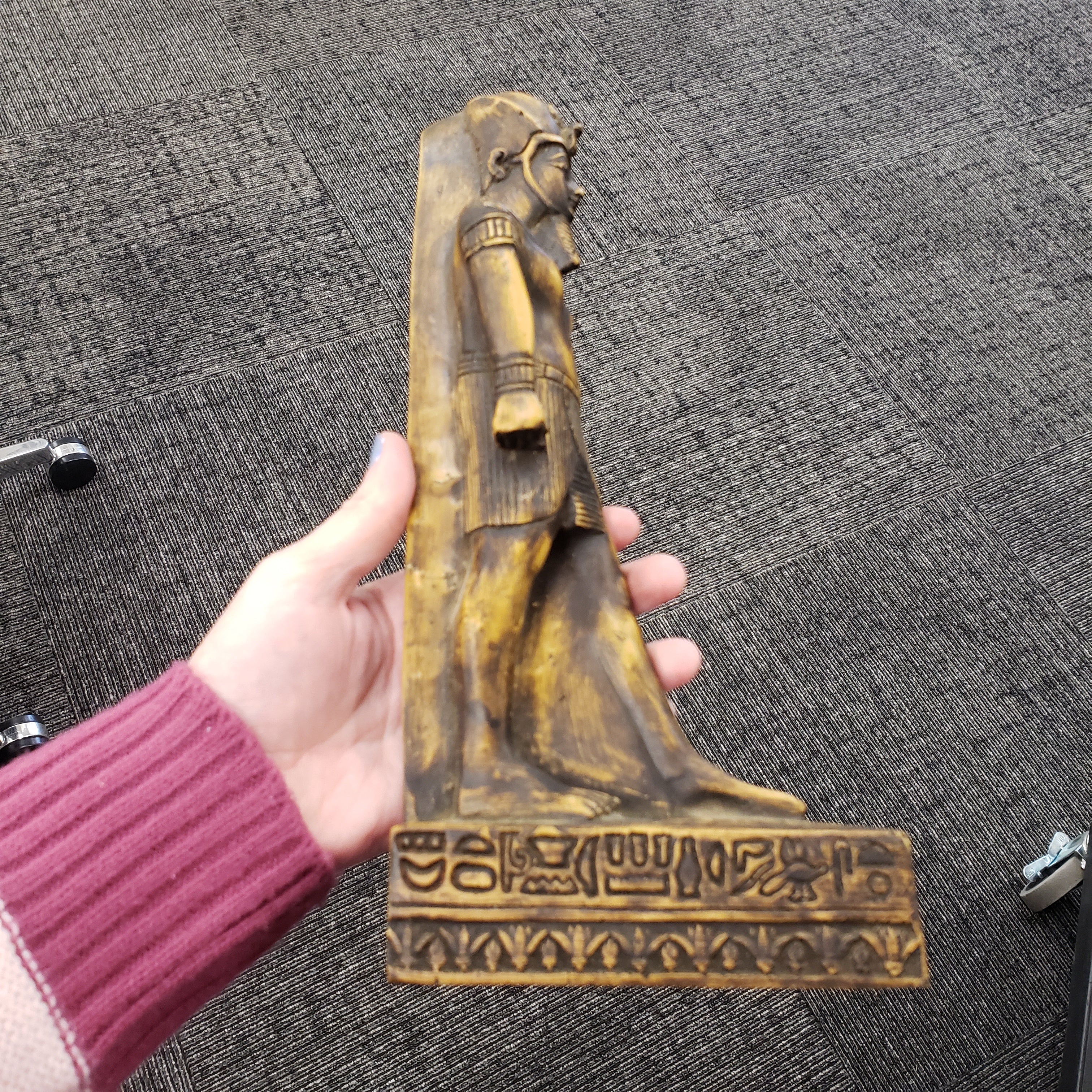 Hand holding a decorative object with hieroglyphics on a textured surface