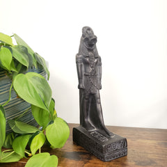 Decorative black Egyptian goddess Sekhmet statue on a wooden surface with a plant in the foreground.