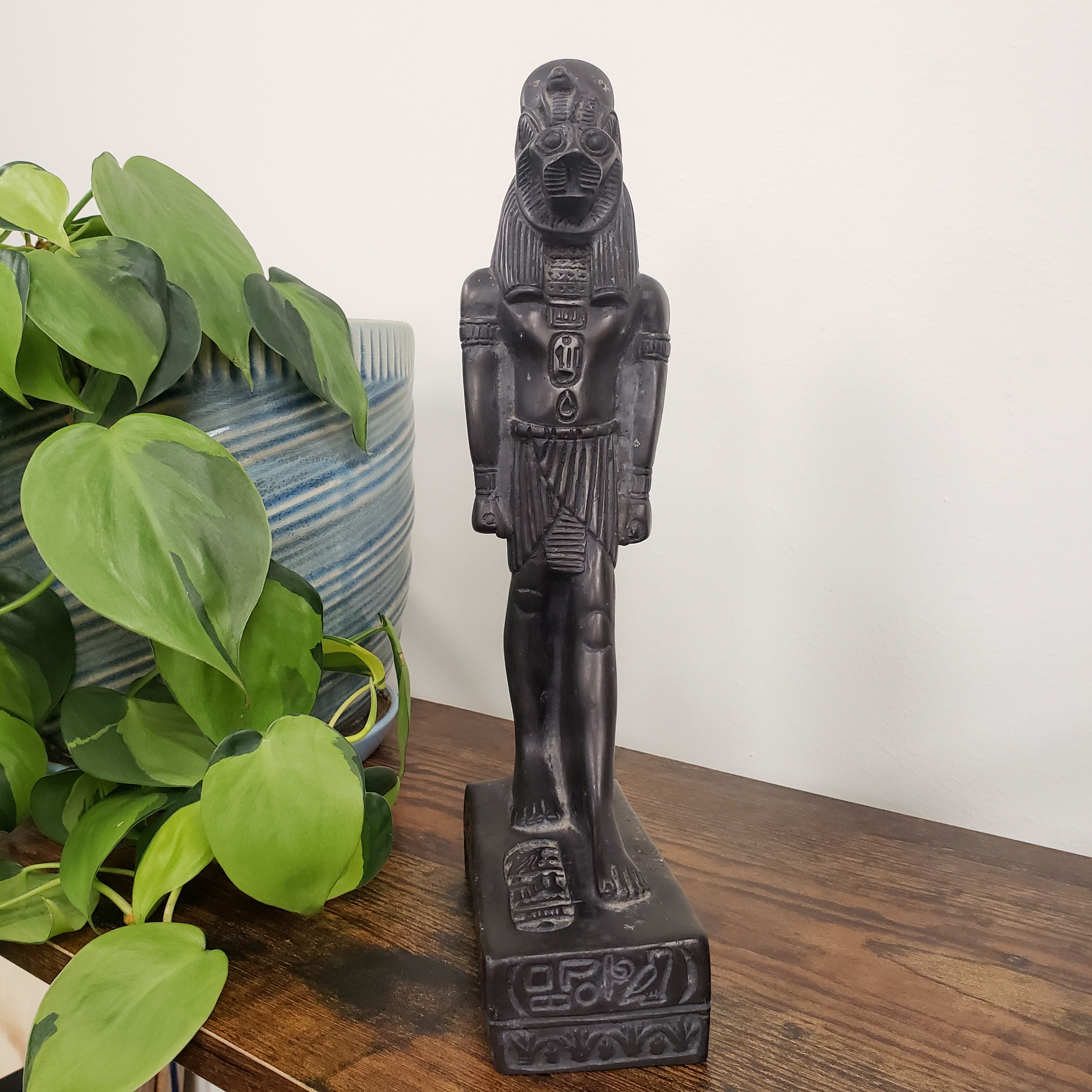 Decorative statue of black Egyptian goddess Sekhmet  on a wooden surface with plants in the foreground