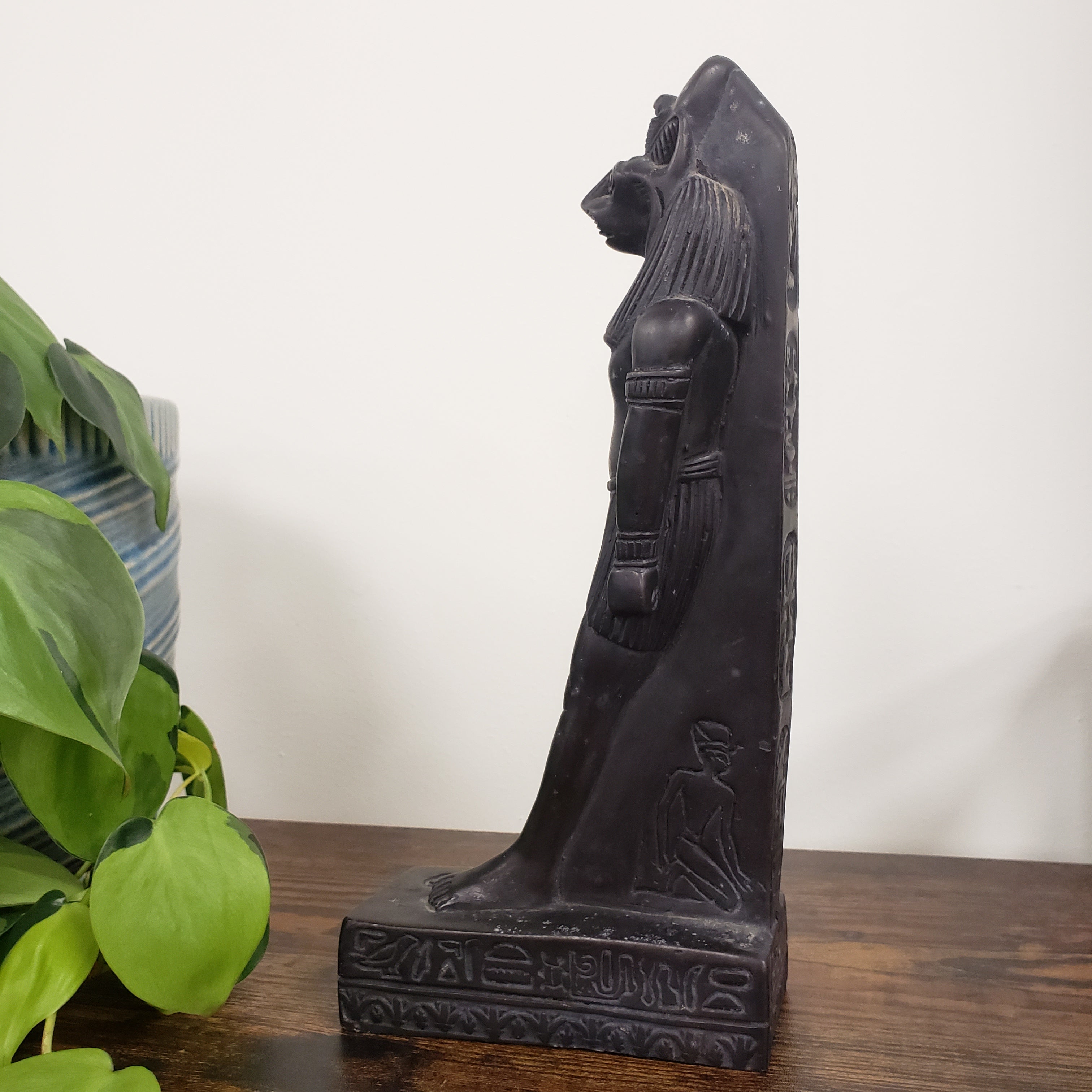 Decorative black black Egyptian goddess Sekhmet statue on a wooden beam with a plant in the foreground