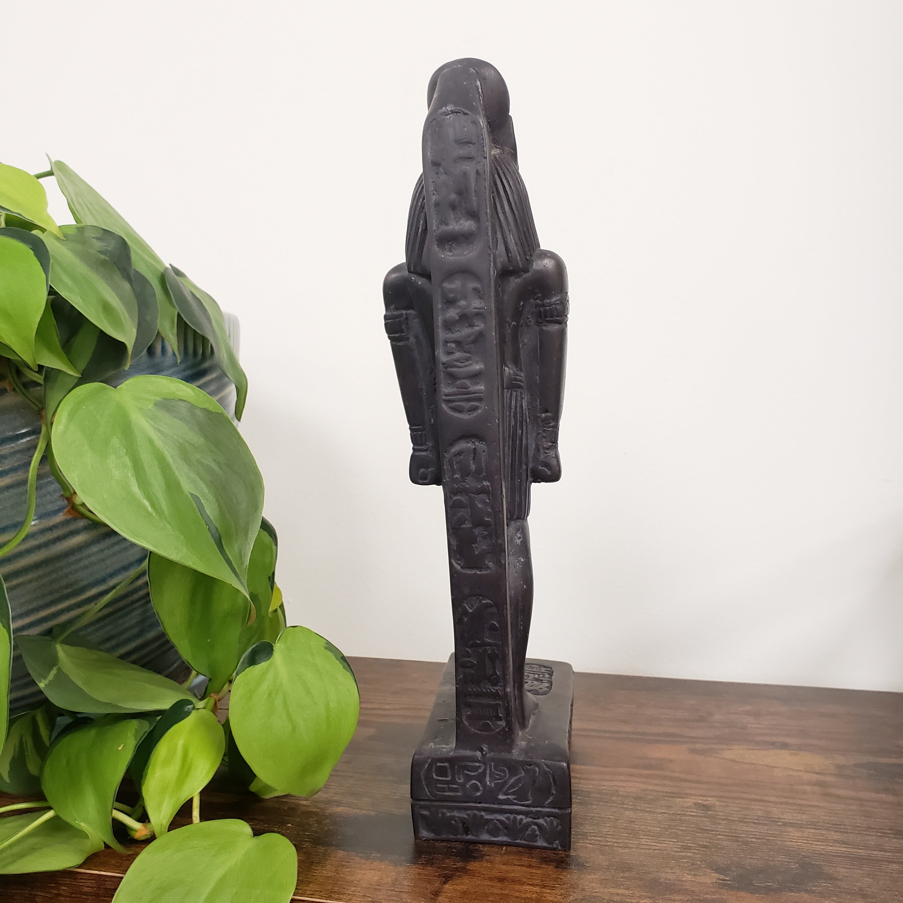 Decorative black Egyptian goddess Sekhmet statue  on a wooden surface with a plant in the foreground