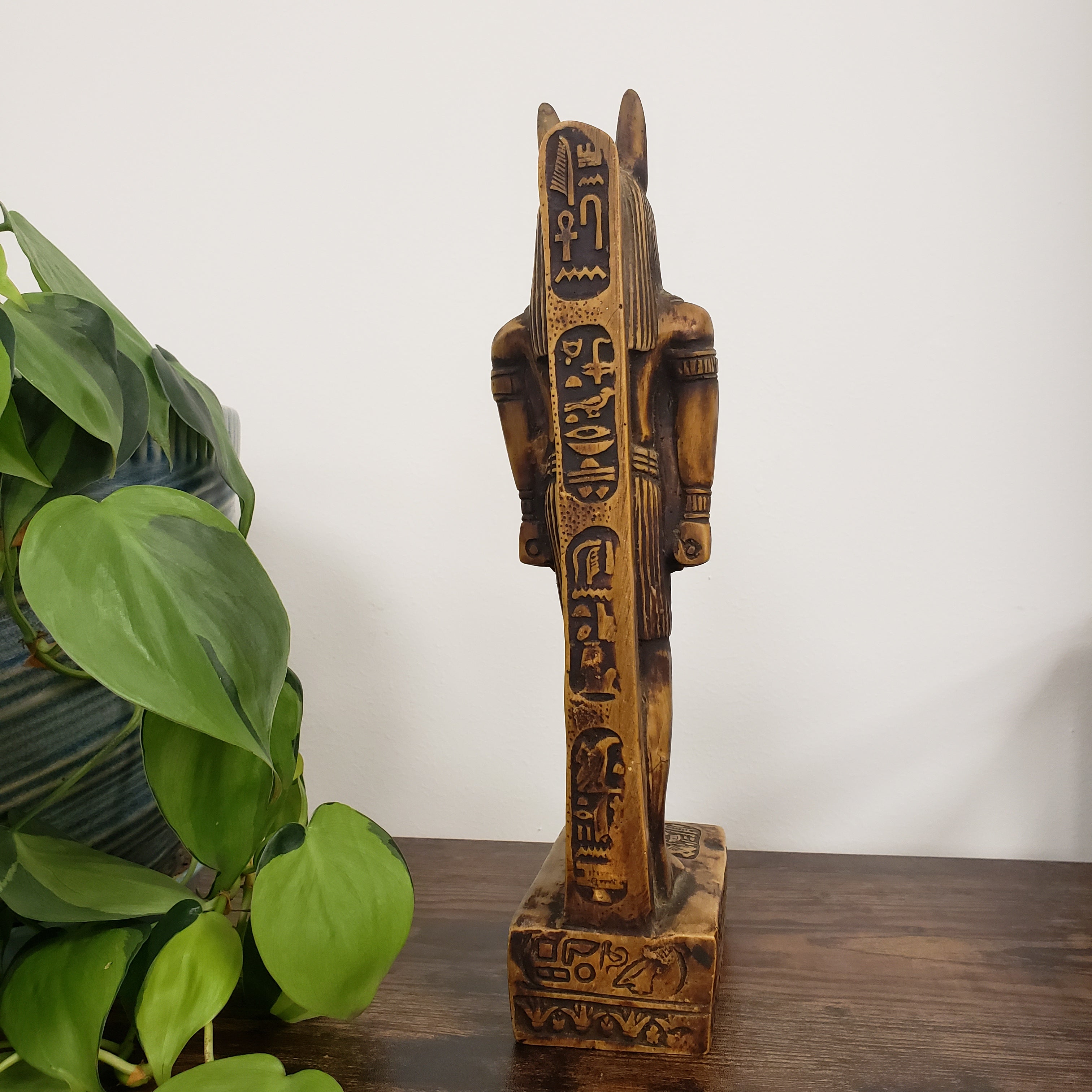Decorative statue of the Egyptian god Anubis with intricate carvings next to a potted plant on a white background