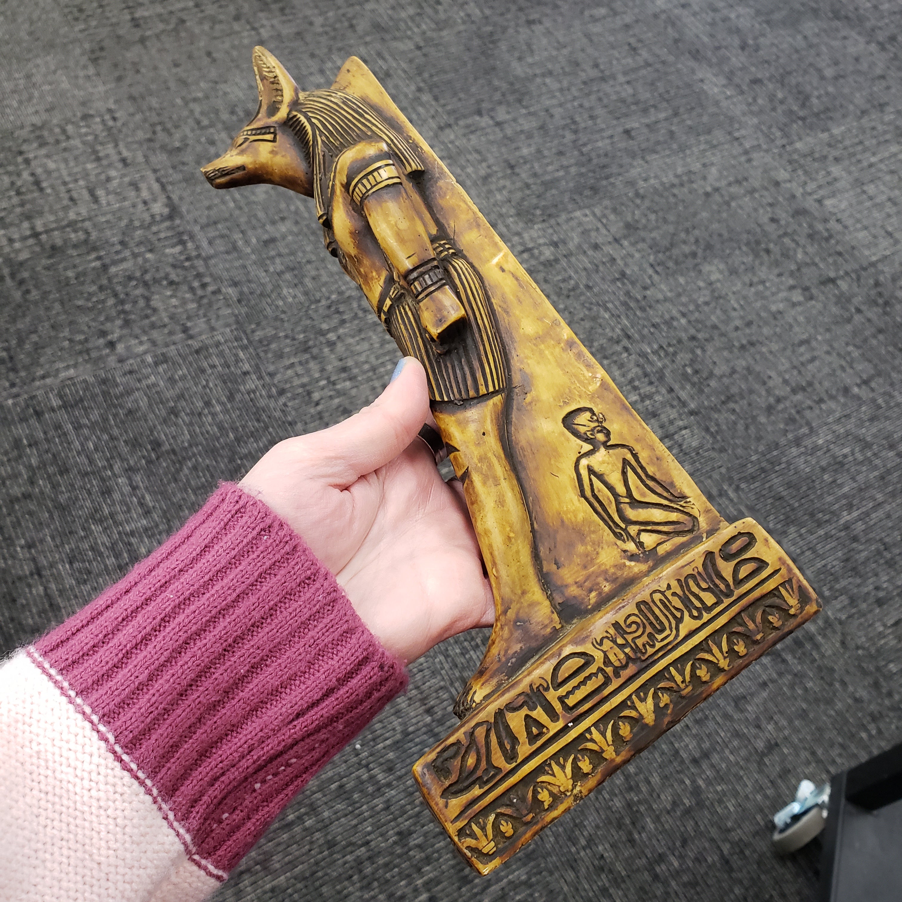 Hand holding a statue of the Egyptian god Anubis with intricate designs against a gray background