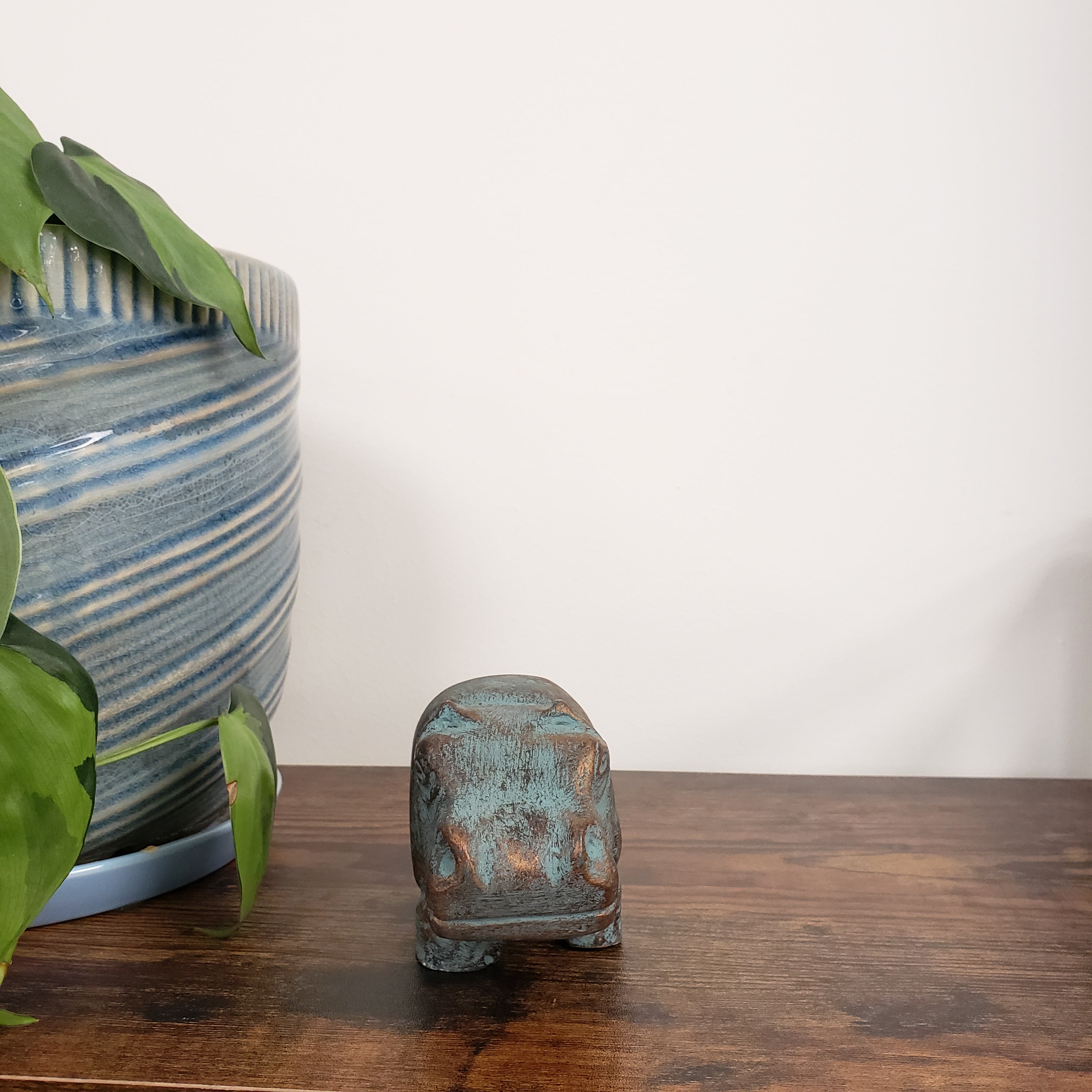 Decorative hippo statue on a wooden shelf and green leaves in the foreground.