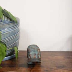 Decorative hippo statue on a wooden shelf and green leaves in the foreground.