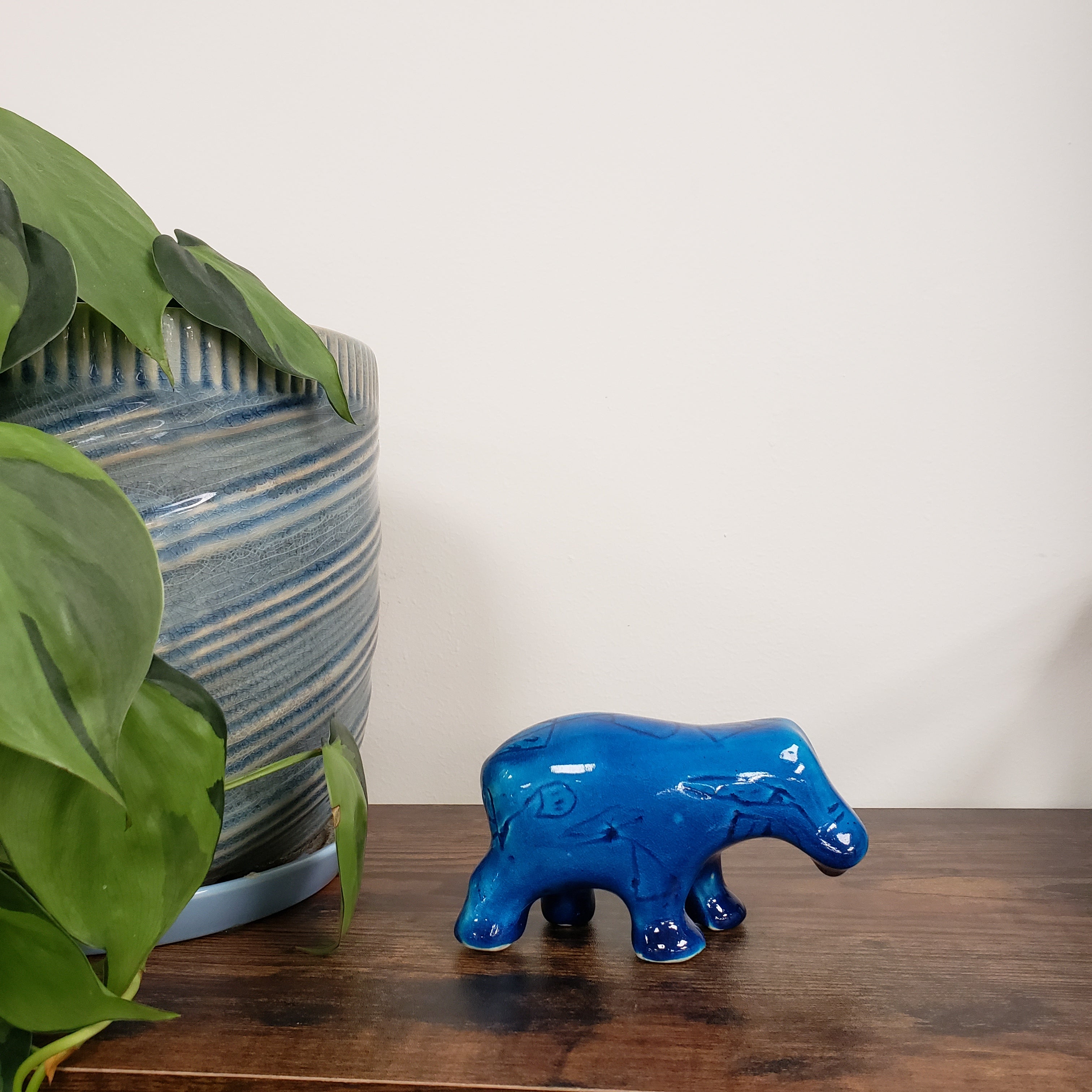 Blue ceramic hippo figurine on a wooden surface with green leaves in the foreground