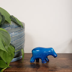 Blue ceramic hippo figurine on a wooden surface with green leaves in the foreground