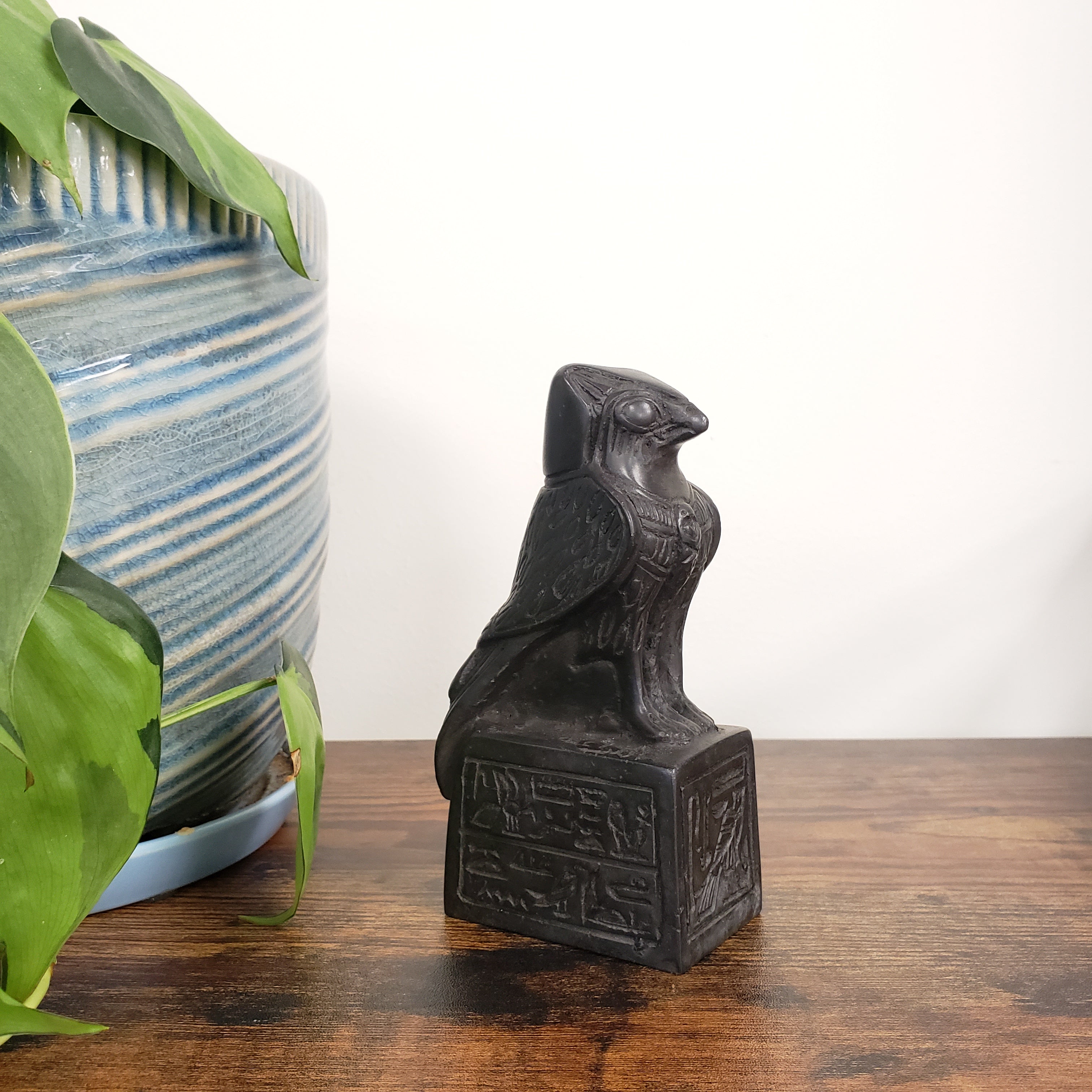 Decorative black bird sculpture on a wooden surface with a plant and striped vase in the background.
