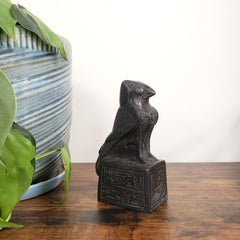 Decorative black bird sculpture on a wooden surface with a plant and striped vase in the background.