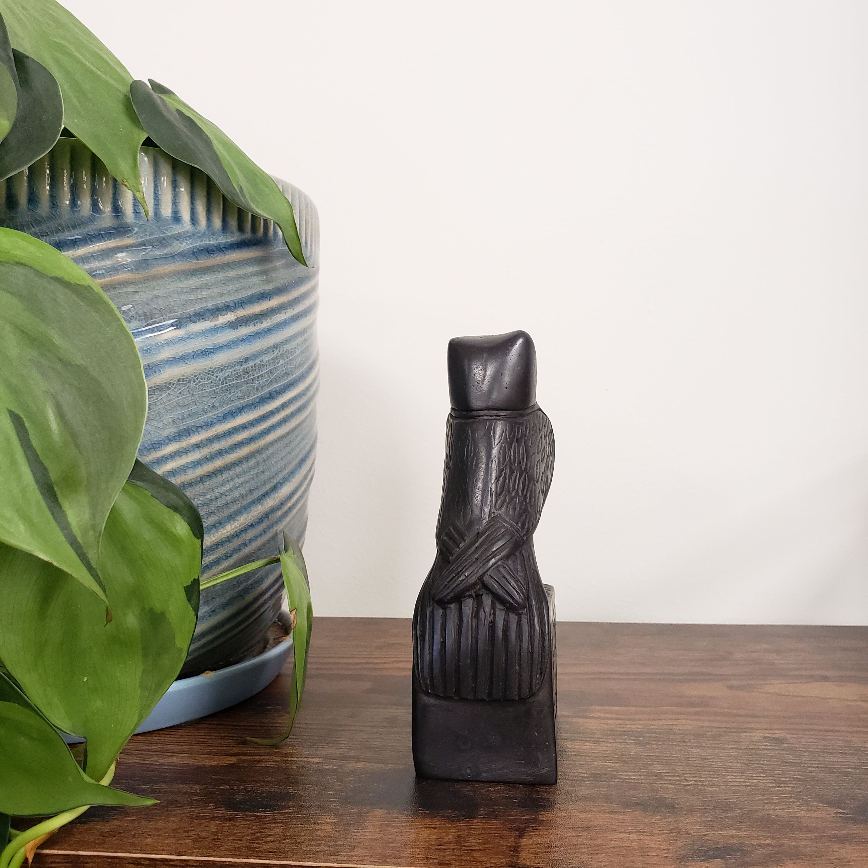 Black decorative falcon on a wooden surface with a plant and blue striped vase in the background
