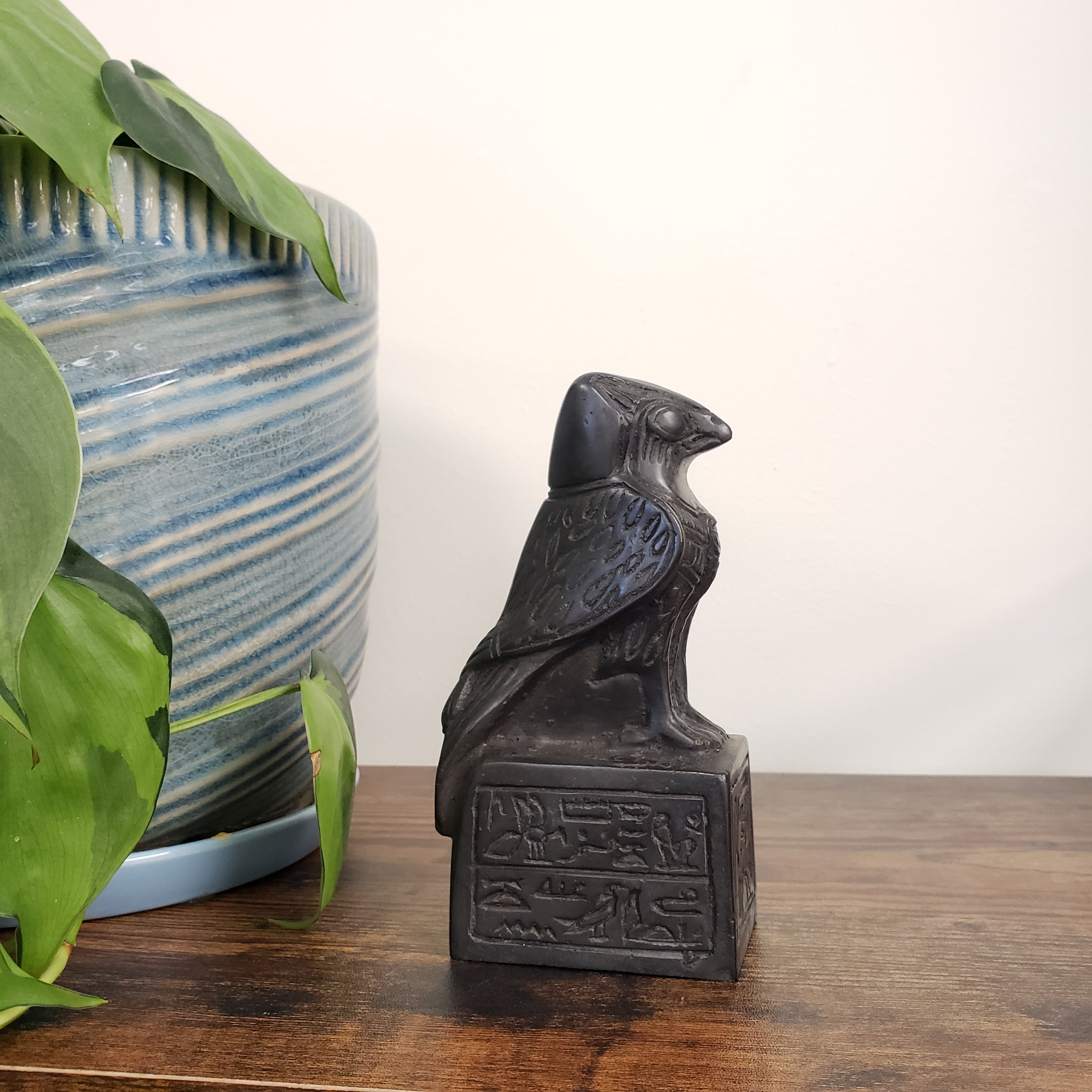 Decorative black falcon on a wooden surface with green leaves in the foreground