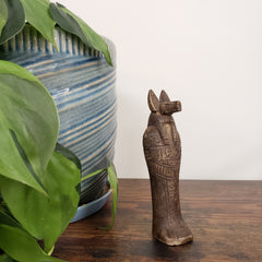 Decorative Egyptian god Anubis statue on a wooden surface with plants and a striped fabric in the background