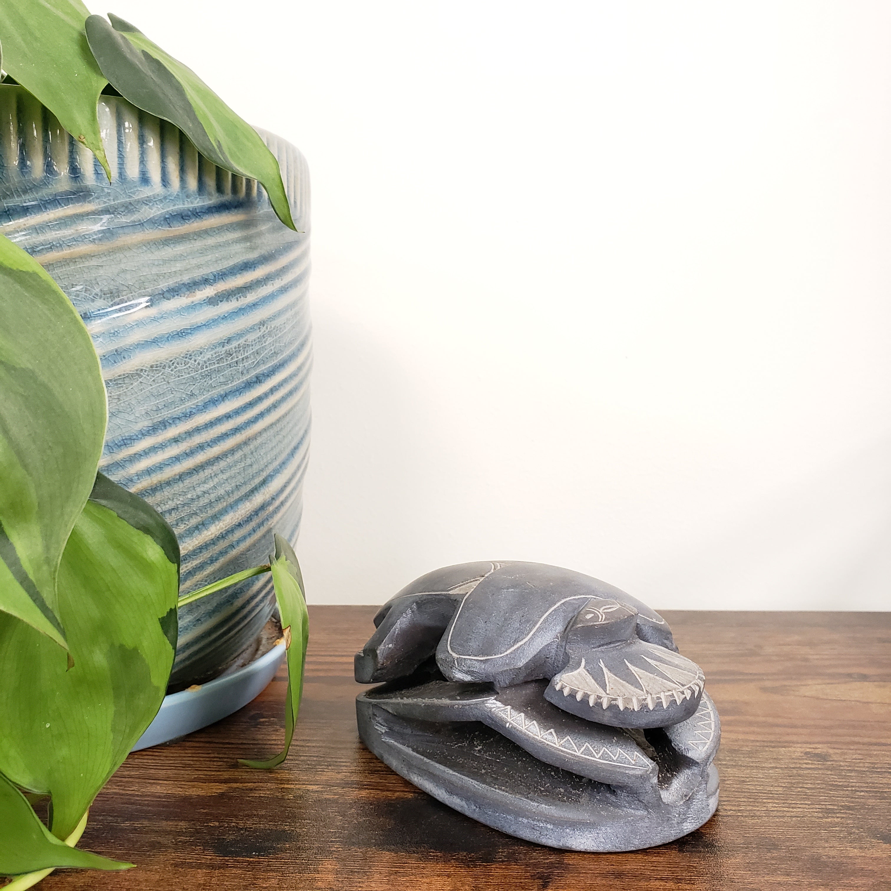 Decorative stone sculpture of a scarab on a wooden wall with plants in the foreground