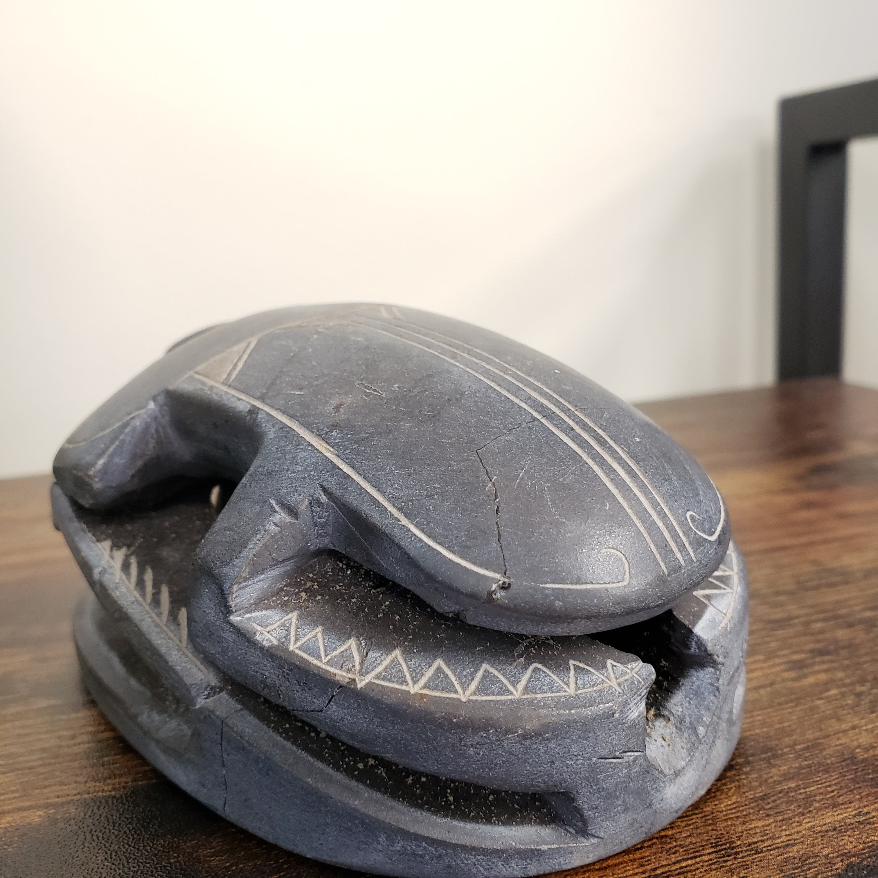 Black sculpture of a scarab with carvings on a wooden surface