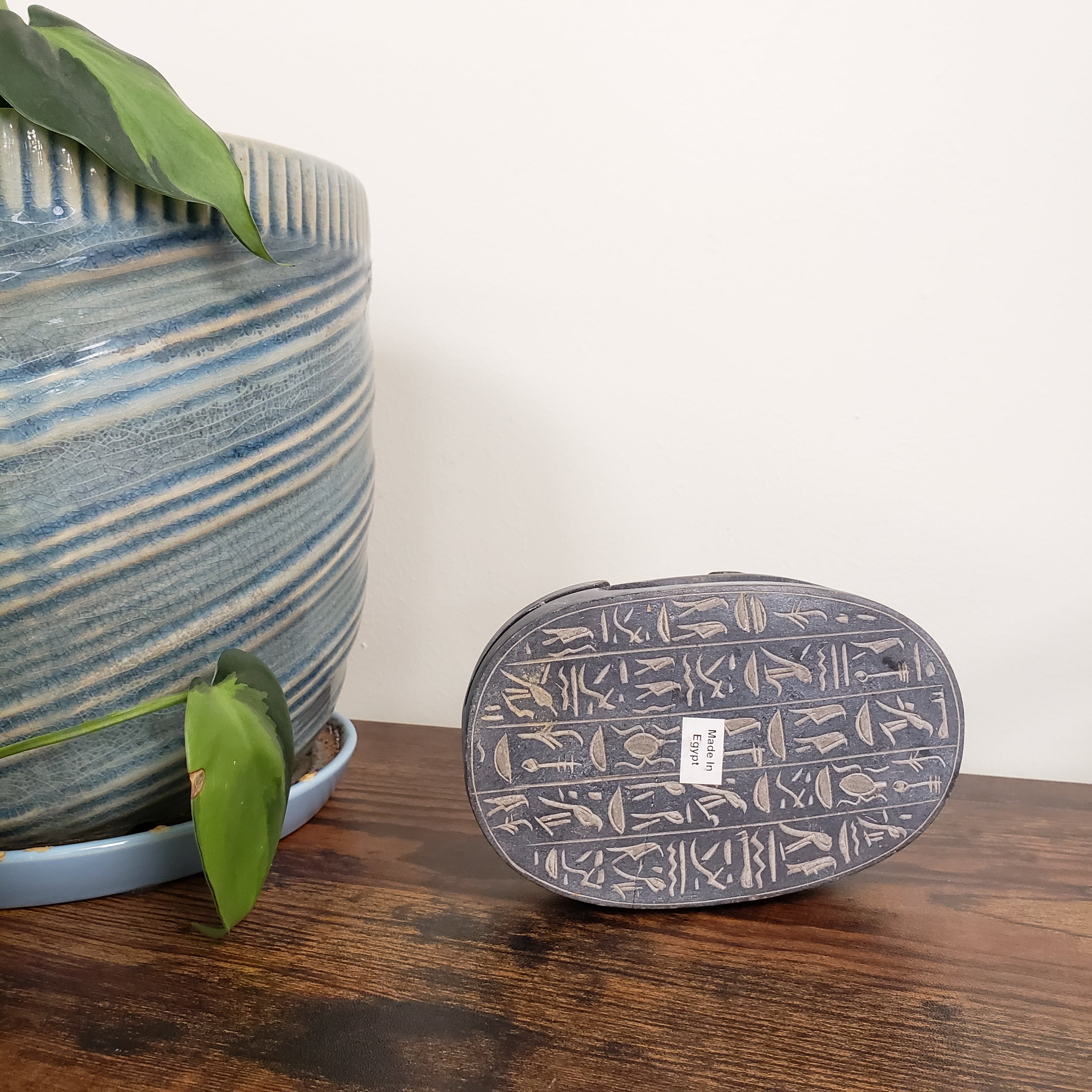 Decorative sculpture of a scarab with hieroglyphics on a wooden surface with a plant in the foreground.
