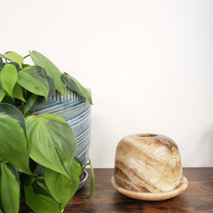Decorative alabaster votive holder on a wooden surface with a plant in the background