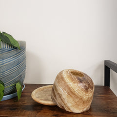Decorative alabaster votive holder on a wooden surface with a plant in the background