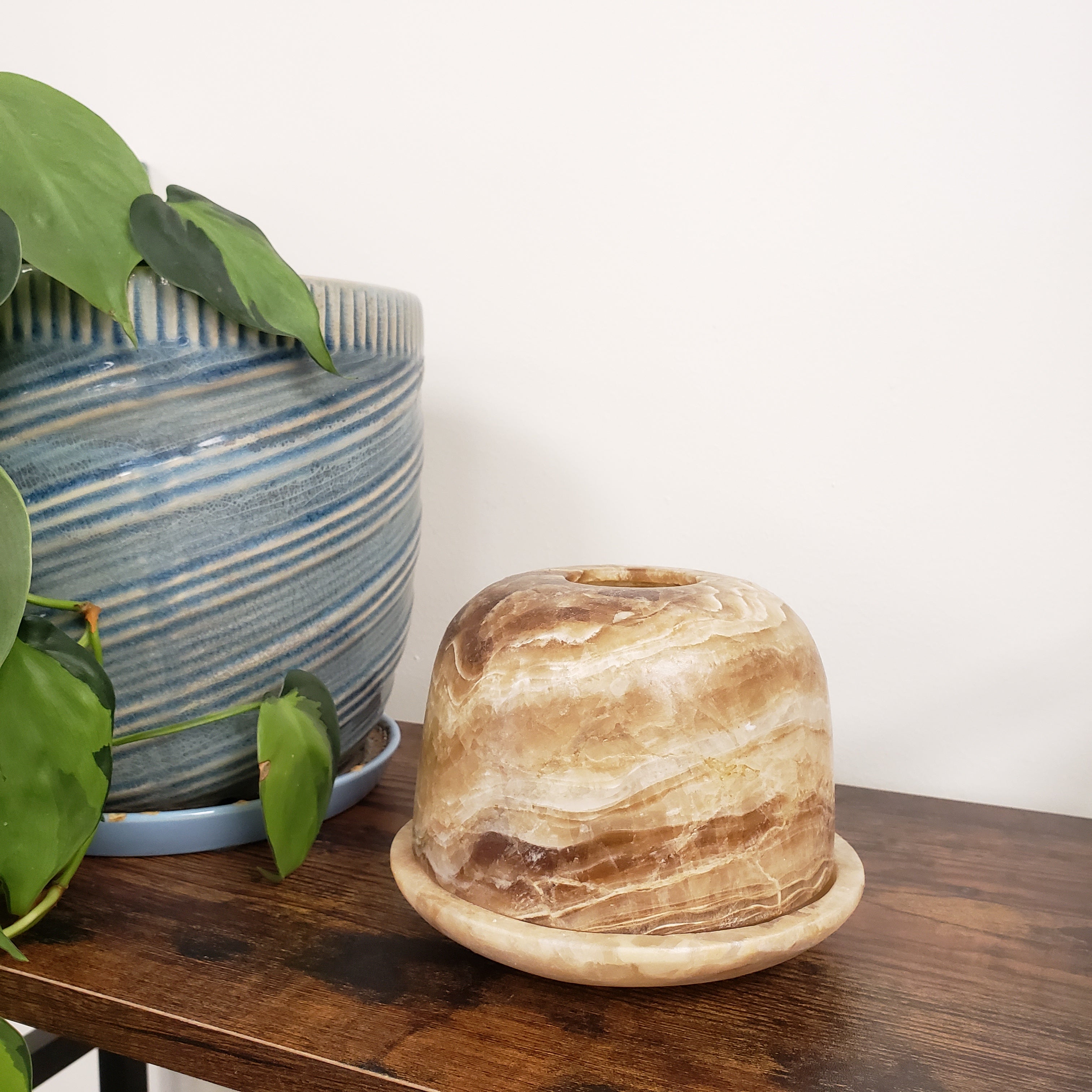 Decorative alabaster votive holder on a white wall with a plant in the foreground