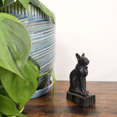 Black cat statue next to a potted plant on a wooden surface