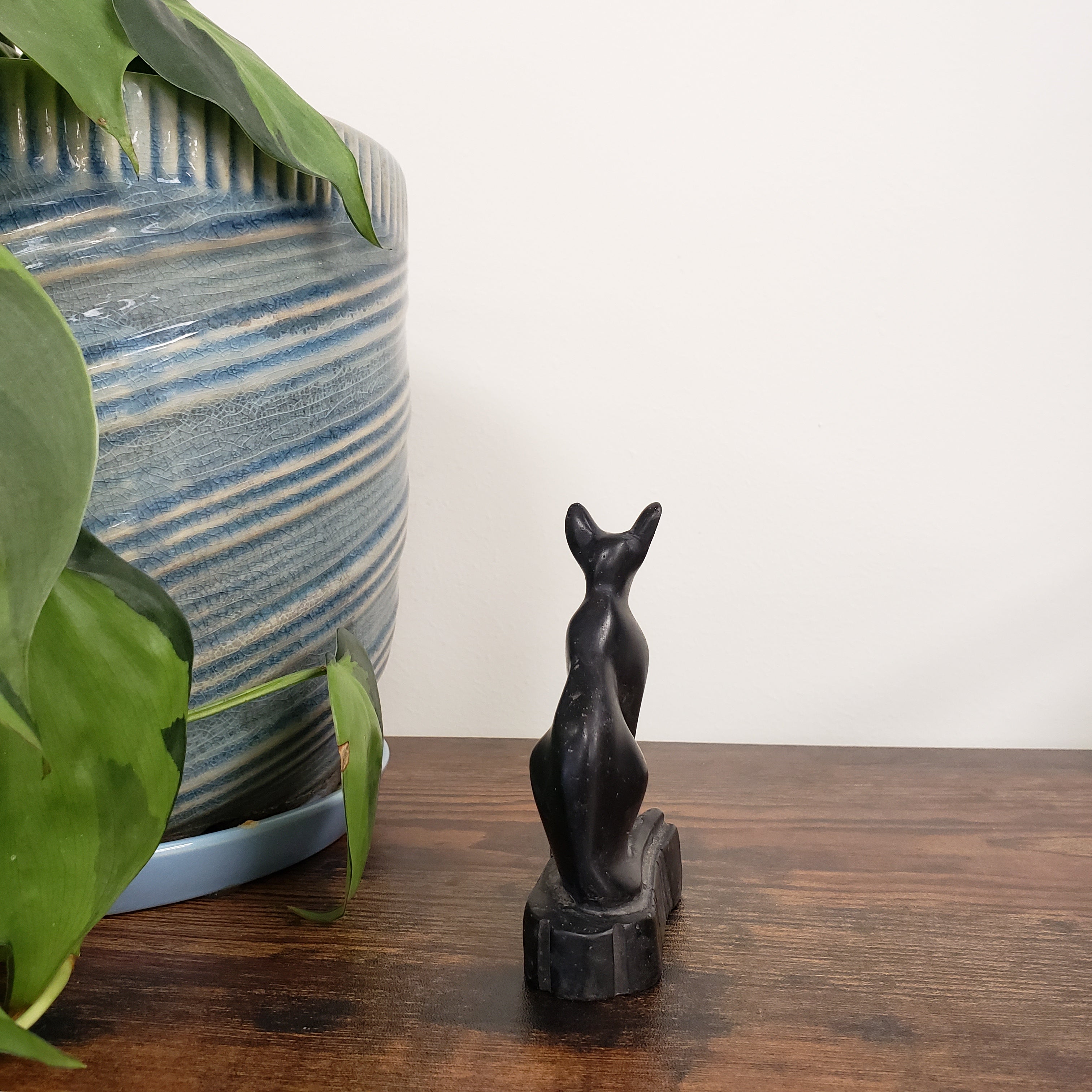 Decorative black cat sculpture with a striped cushion and plant in the foreground.
