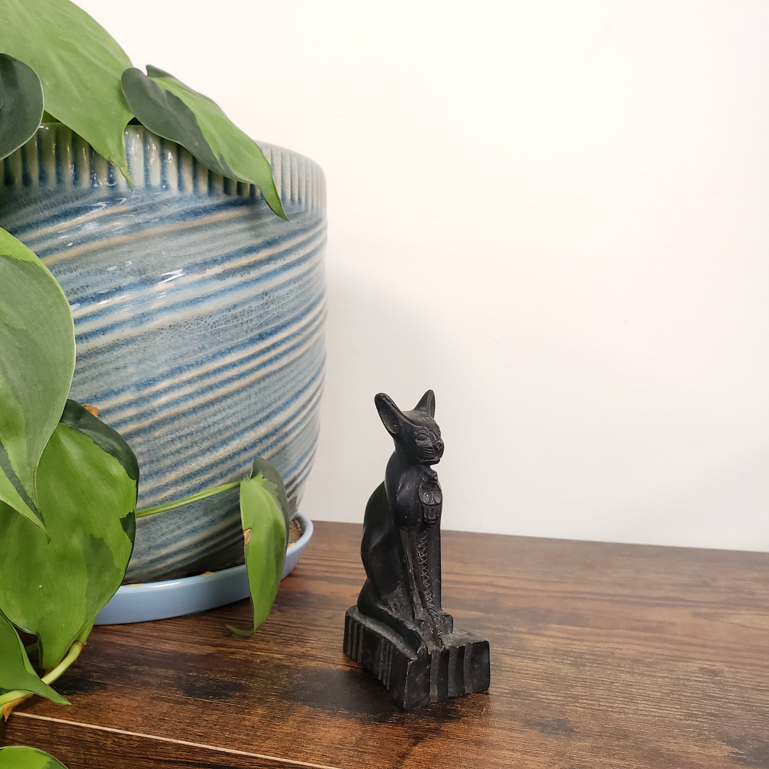 Black cat figurine next to a potted plant on a wooden surface